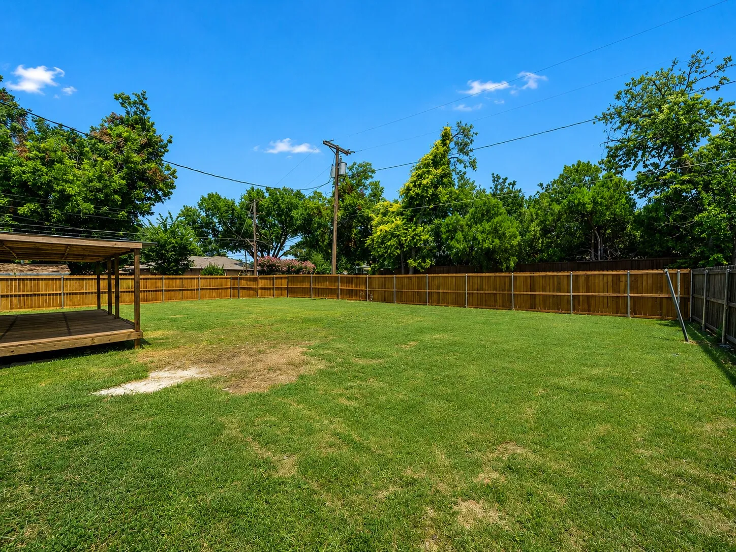 Expansive backyard featuring a large lawn, wood privacy fencing, and a built-in wooden deck with an overhead structure