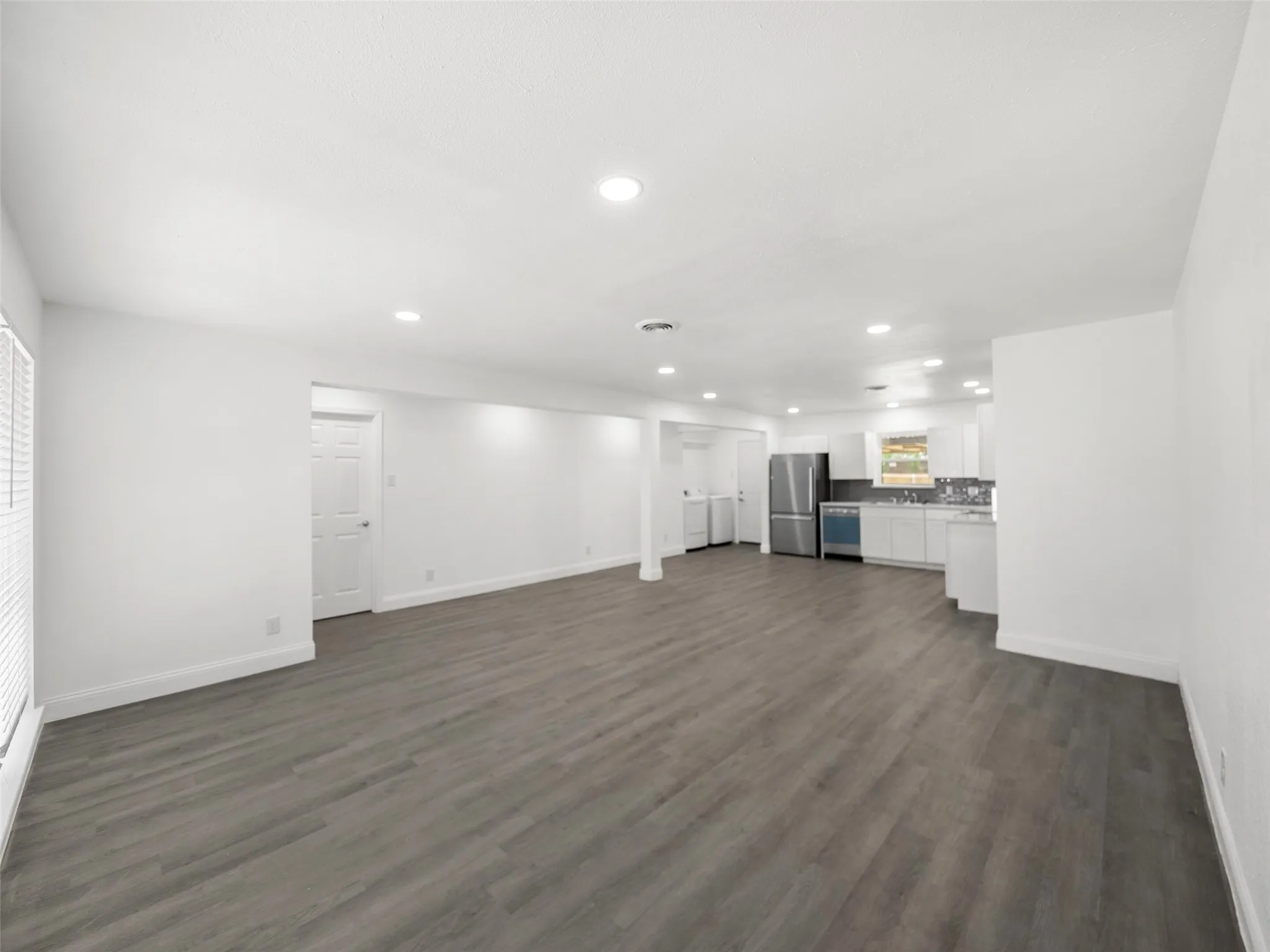 Open-concept living space featuring wood-finish flooring, recessed lighting, and a kitchen with stainless steel appliances, white cabinetry, and a tile backsplash
