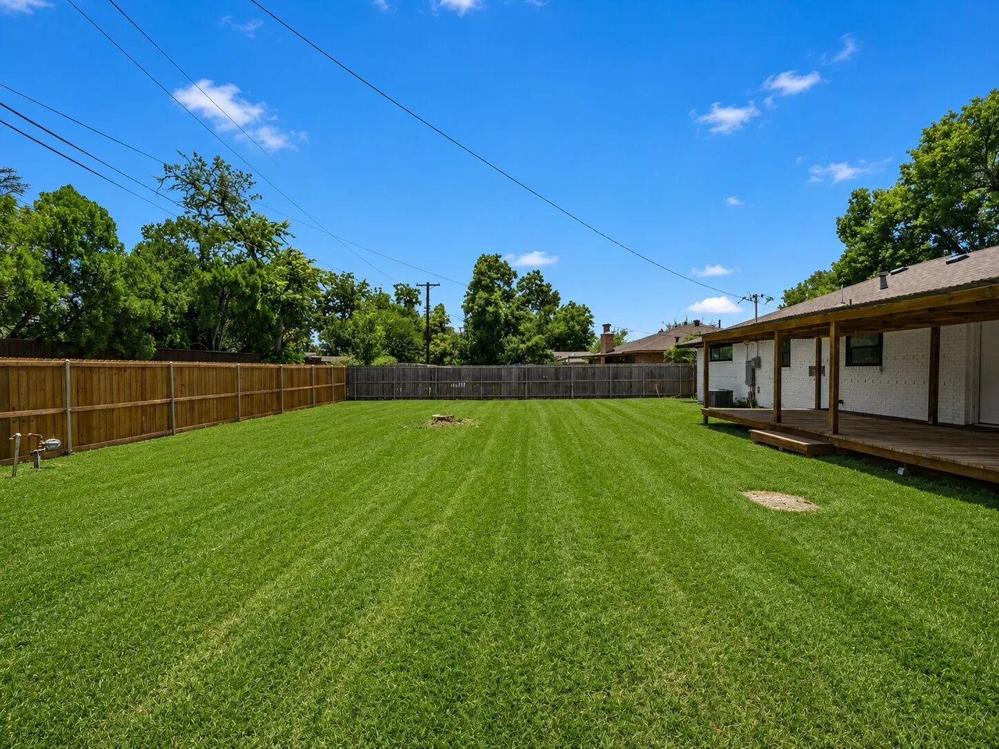 Expansive backyard featuring a manicured lawn, wood privacy fencing, and a covered wood deck