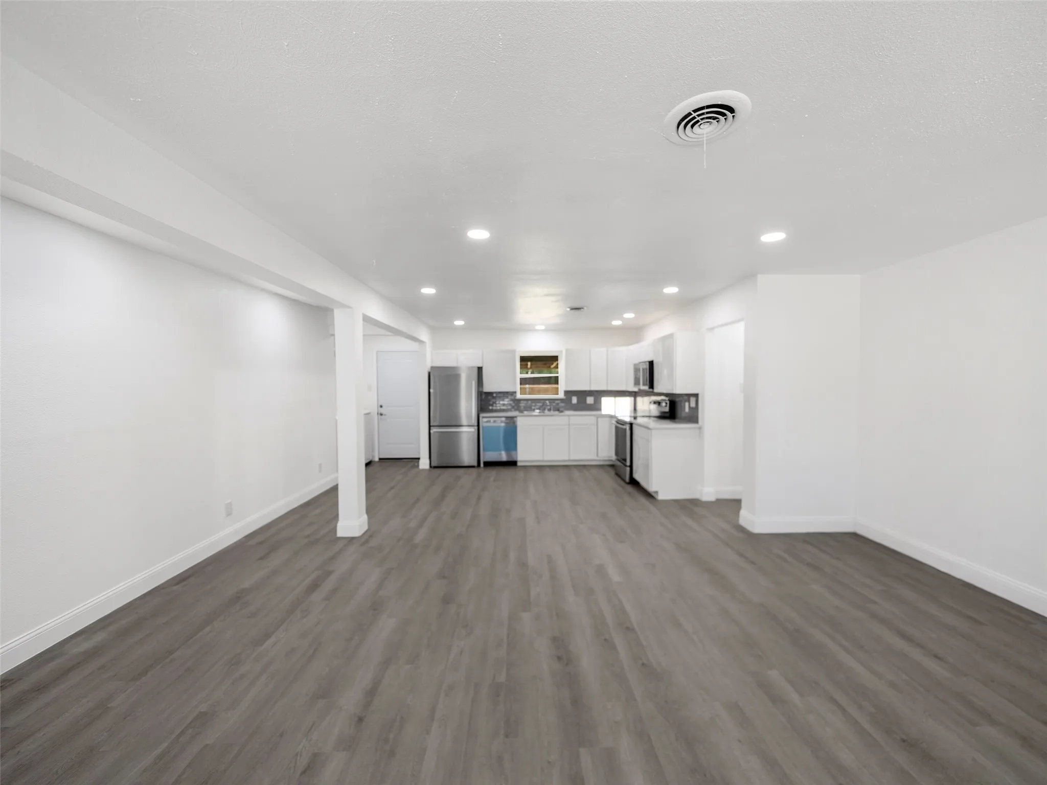 Open-concept living area with wood-finish flooring, recessed lighting, white walls, and a kitchen featuring white cabinetry and stainless steel appliances