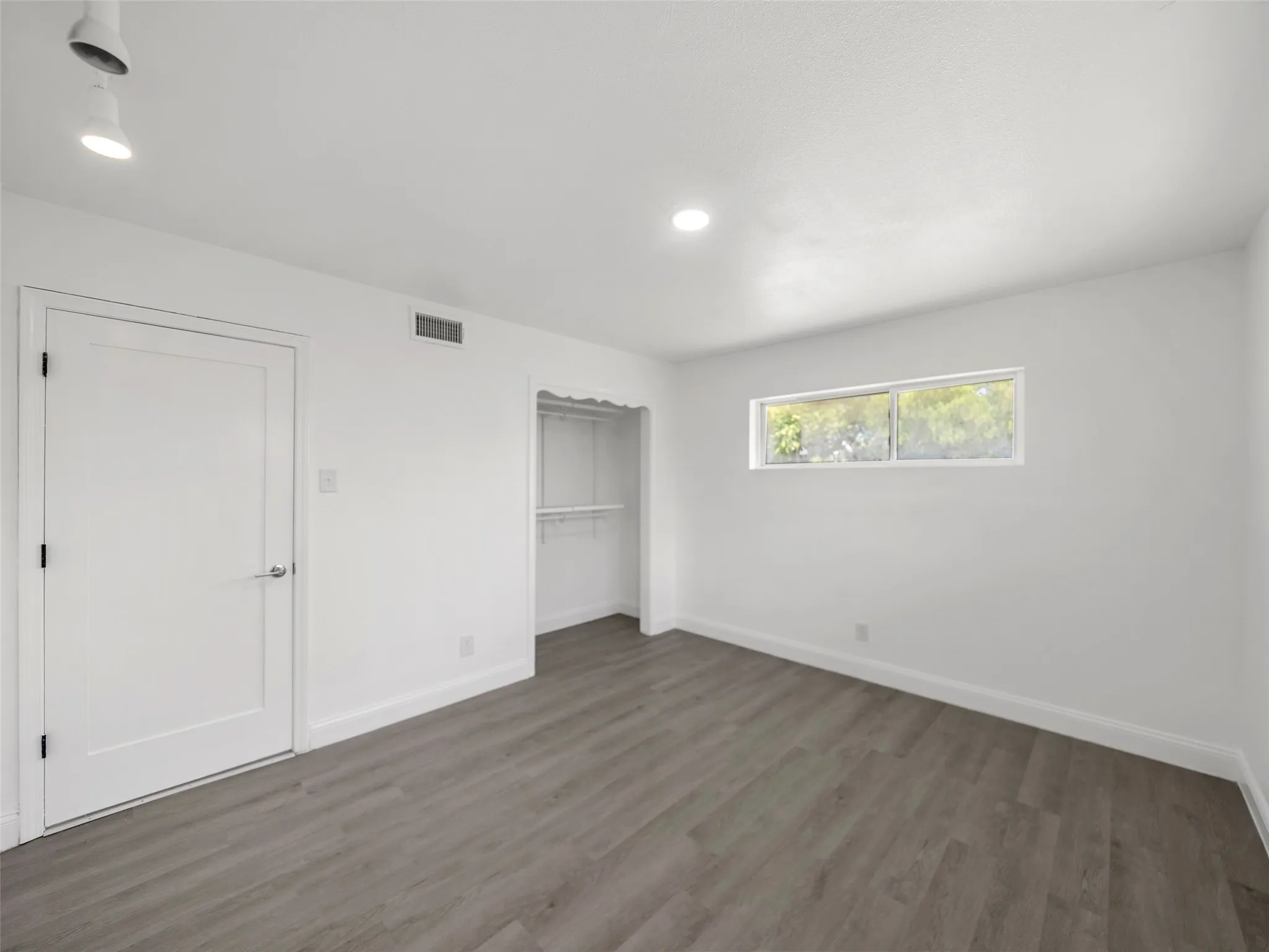 Wood-finish flooring, recessed lighting, track lighting, horizontal window, and an open closet with shelving