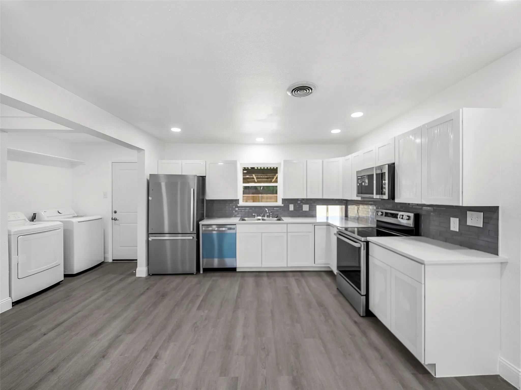 Kitchen featuring white shaker cabinetry, stainless steel appliances, light countertops, and gray subway tile backsplash