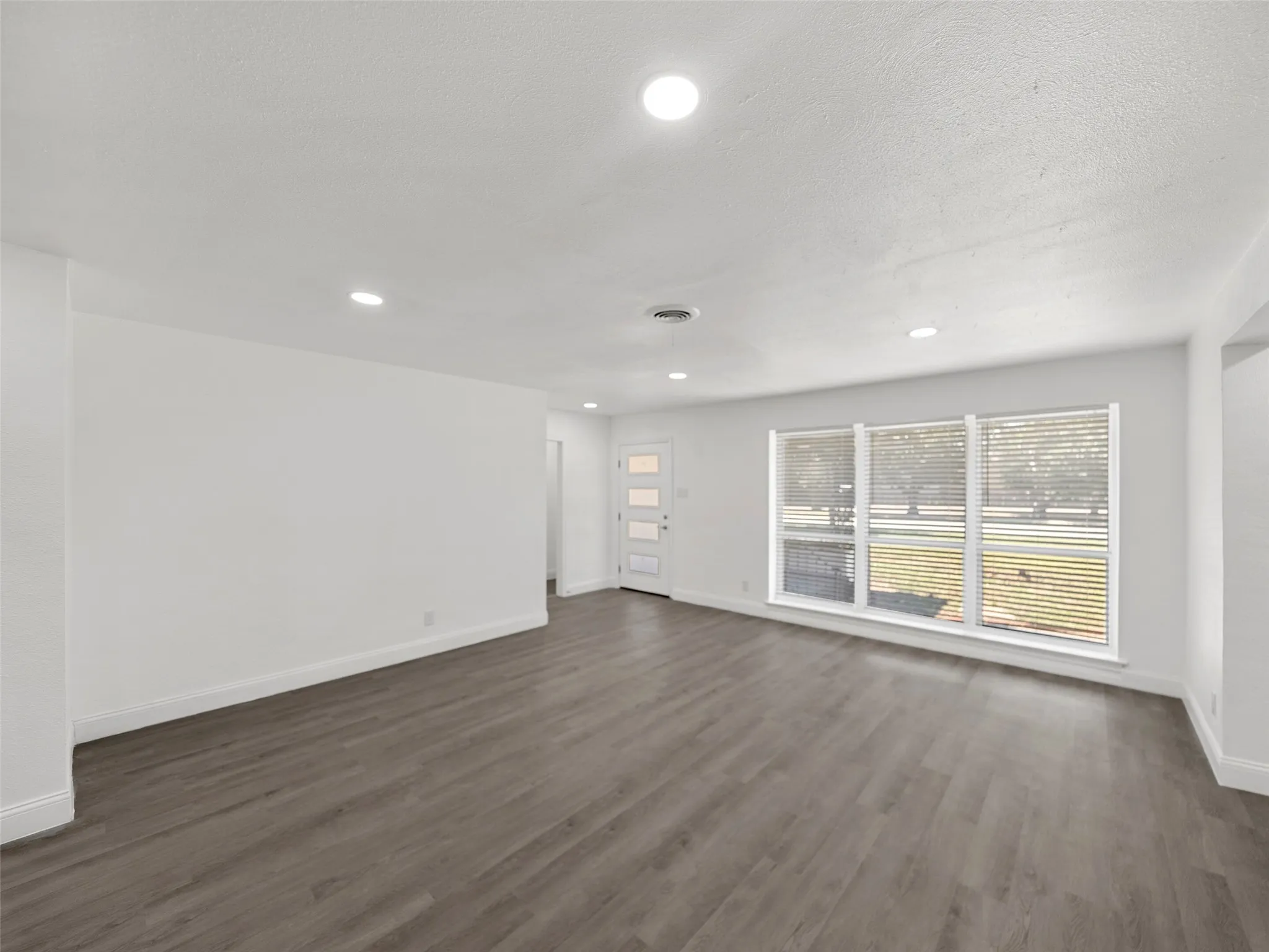 Spacious living area featuring wood-finish flooring, recessed lighting, and large windows with blinds