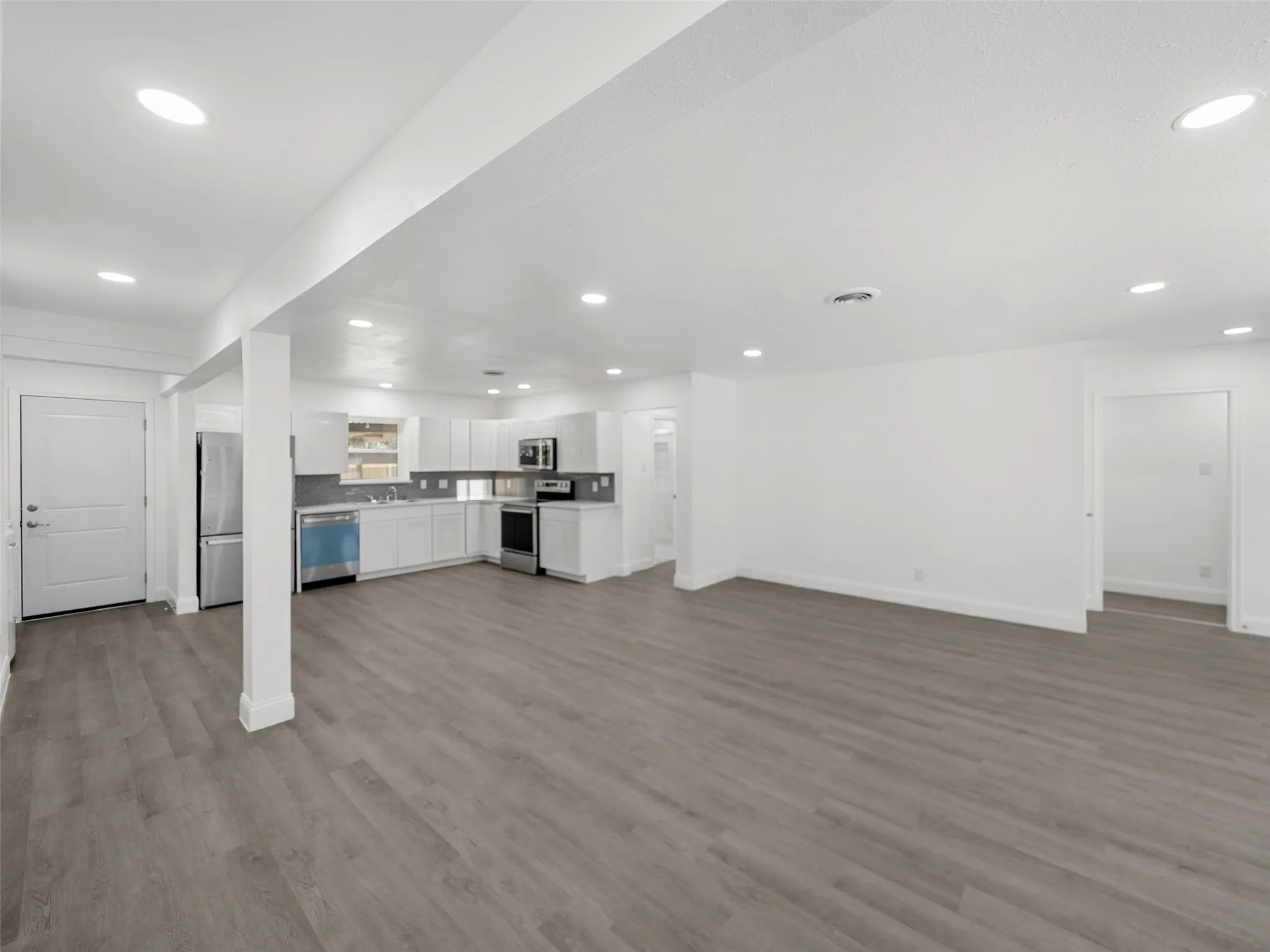 Open-concept living space featuring wood-finish flooring, recessed lighting, and a kitchen with white cabinetry, stainless steel appliances, and a tiled backsplash
