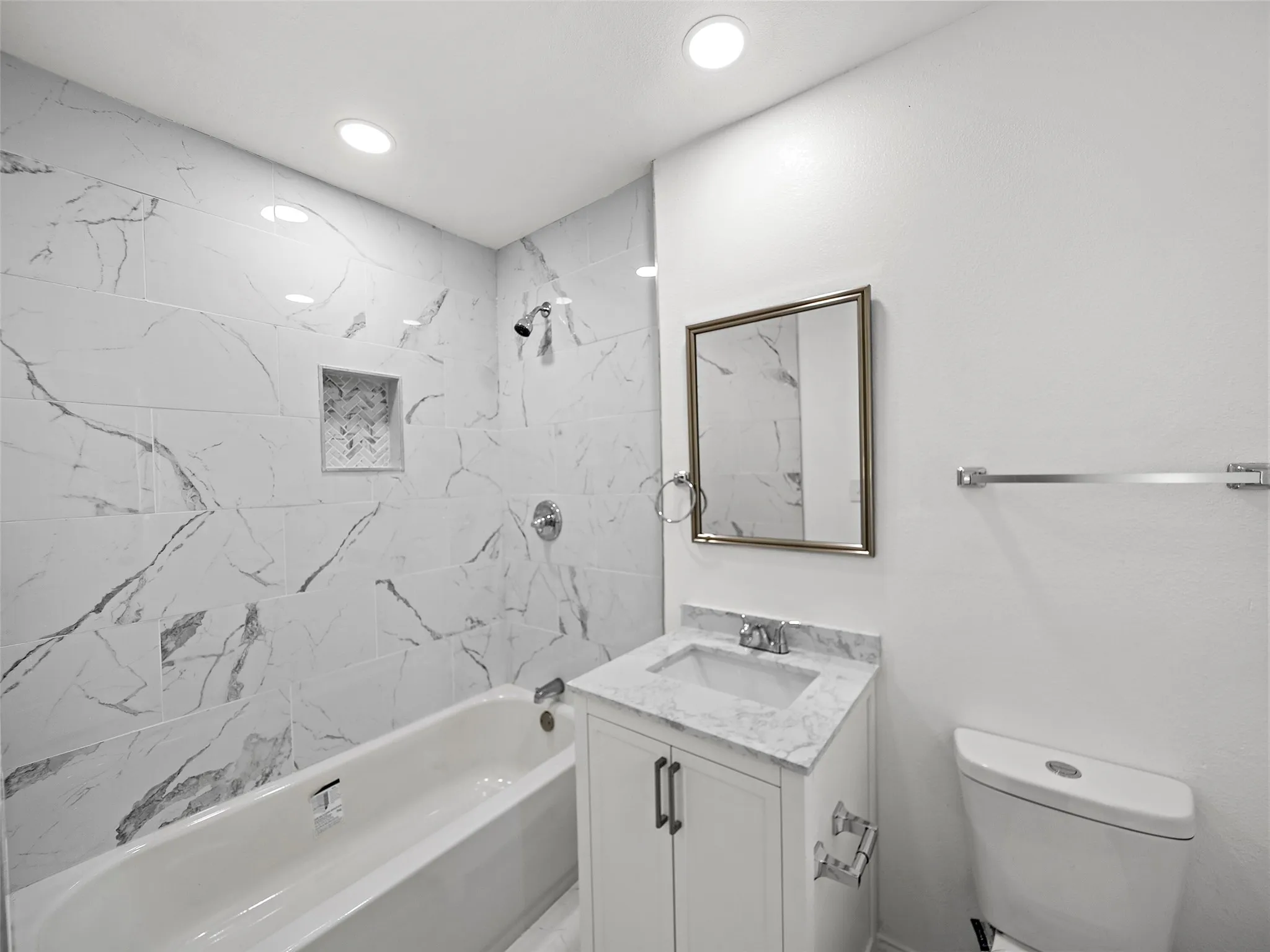 Recessed lighting illuminates the white bathtub and shower featuring white and gray patterned tile