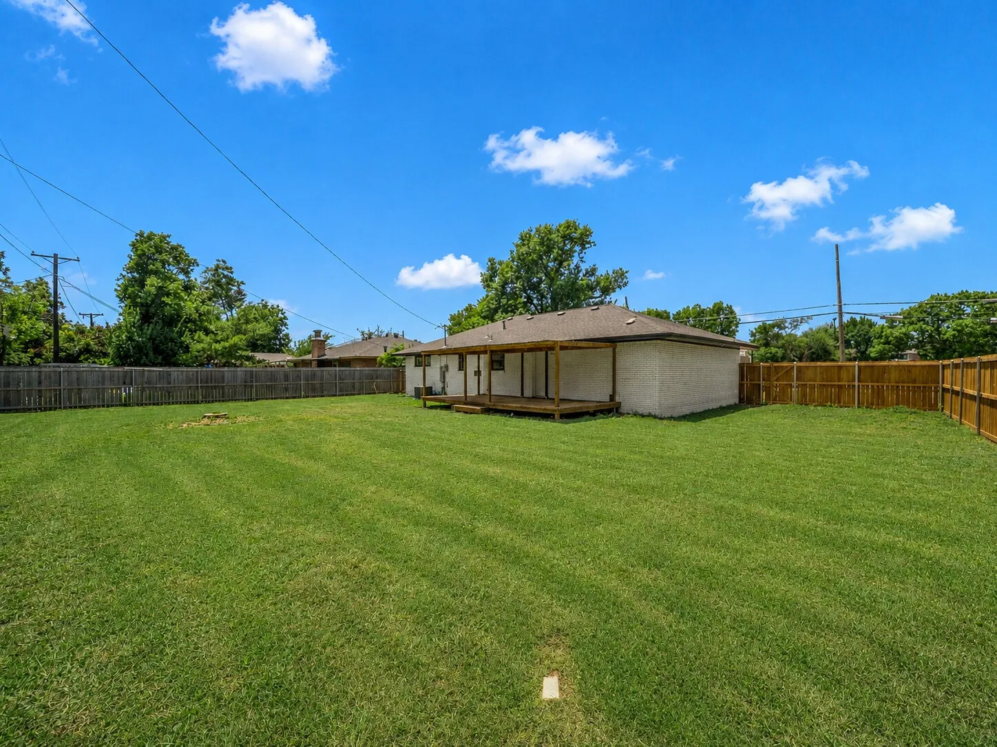 Expansive backyard with a manicured lawn, full wood fencing, and a covered wood deck