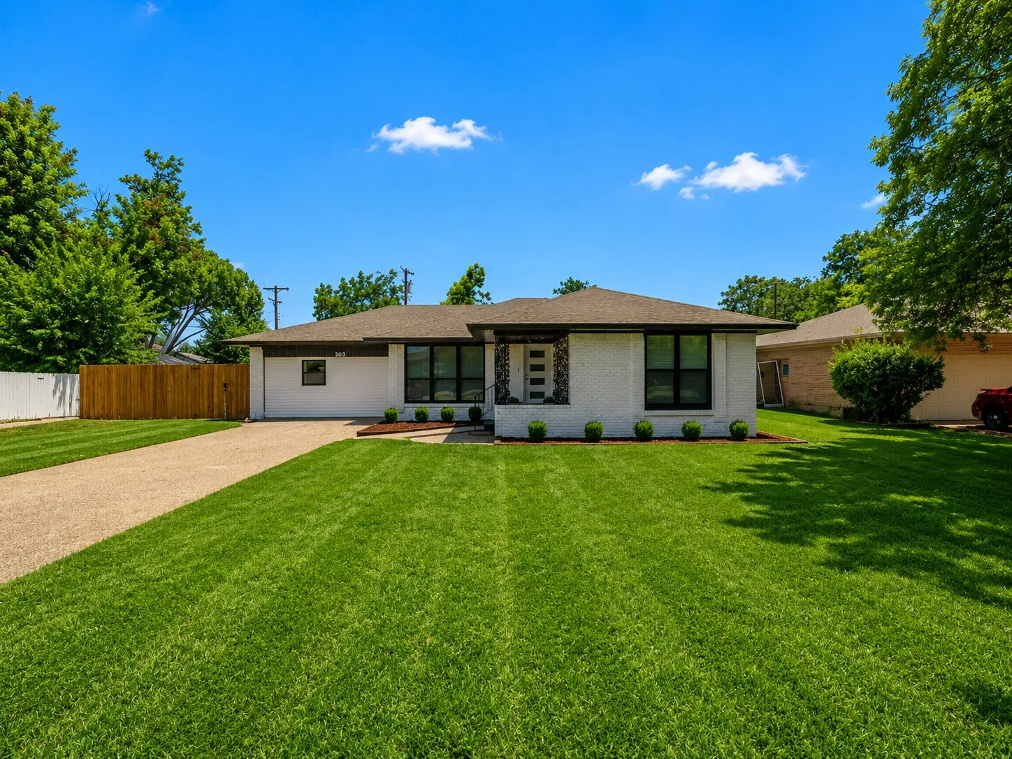 Brick exterior with dark-framed windows, a large front lawn, a gravel driveway, and a wooden privacy fence
