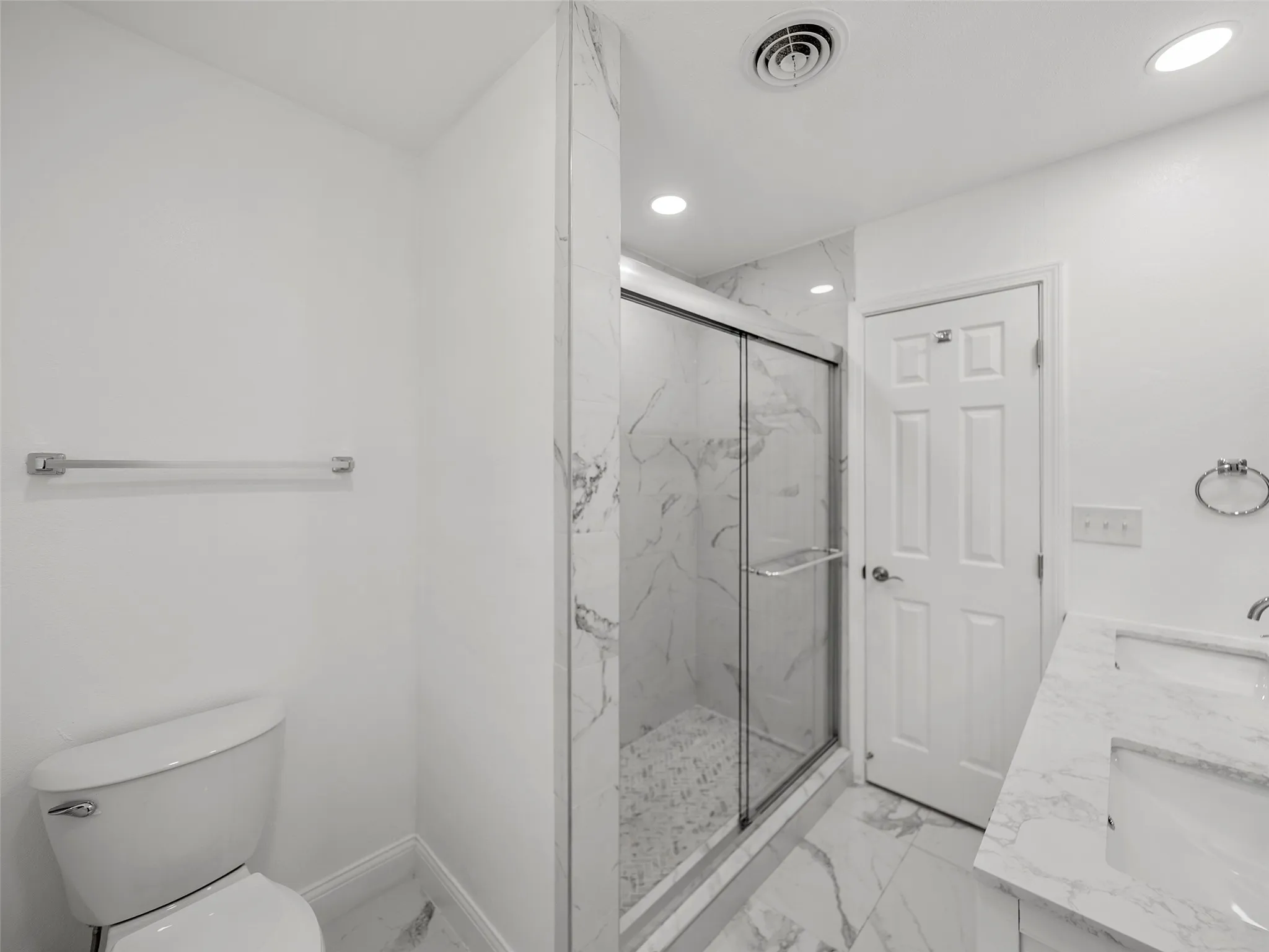 Walk-in shower with glass enclosure, dual vanity with undermount sinks, and marble-look tile flooring