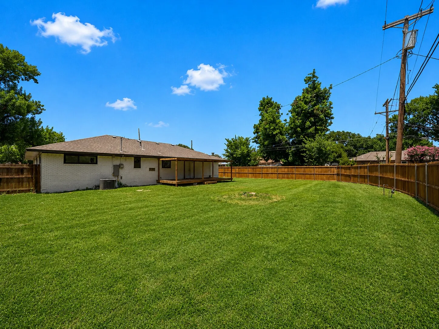 Expansive rear yard featuring green grass, a wood privacy fence, and a rear deck
