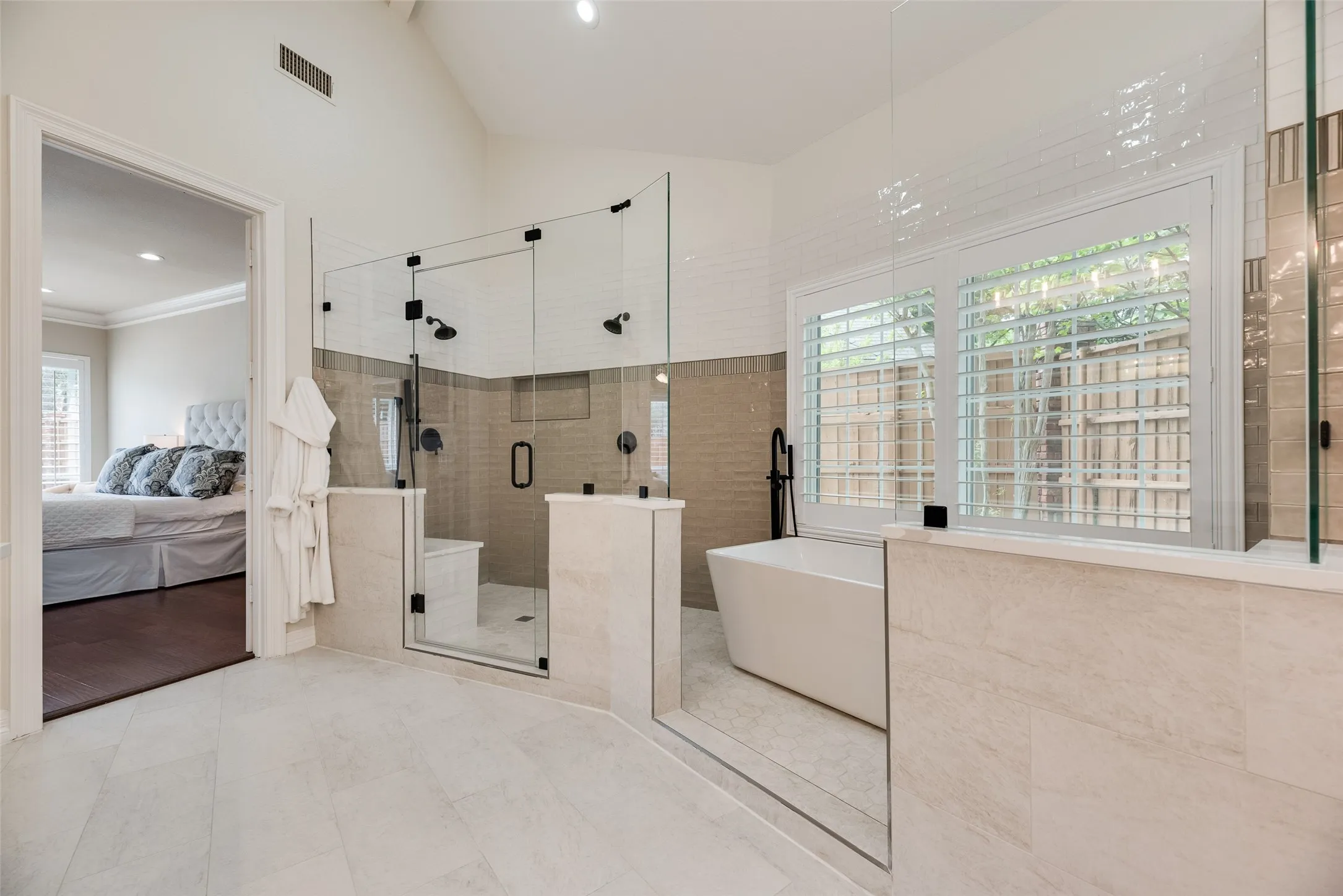 Spacious bathroom featuring a freestanding tub, glass-enclosed shower with dual showerheads, and light-toned tile flooring