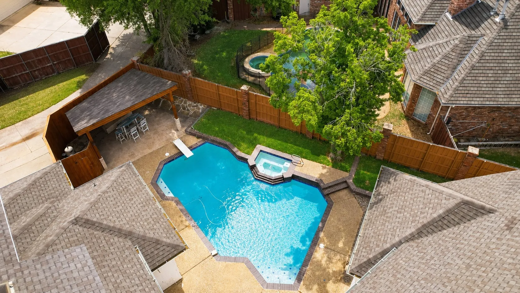 Backyard featuring a swimming pool with integrated spa, diving board, covered patio, privacy fencing, and manicured lawn