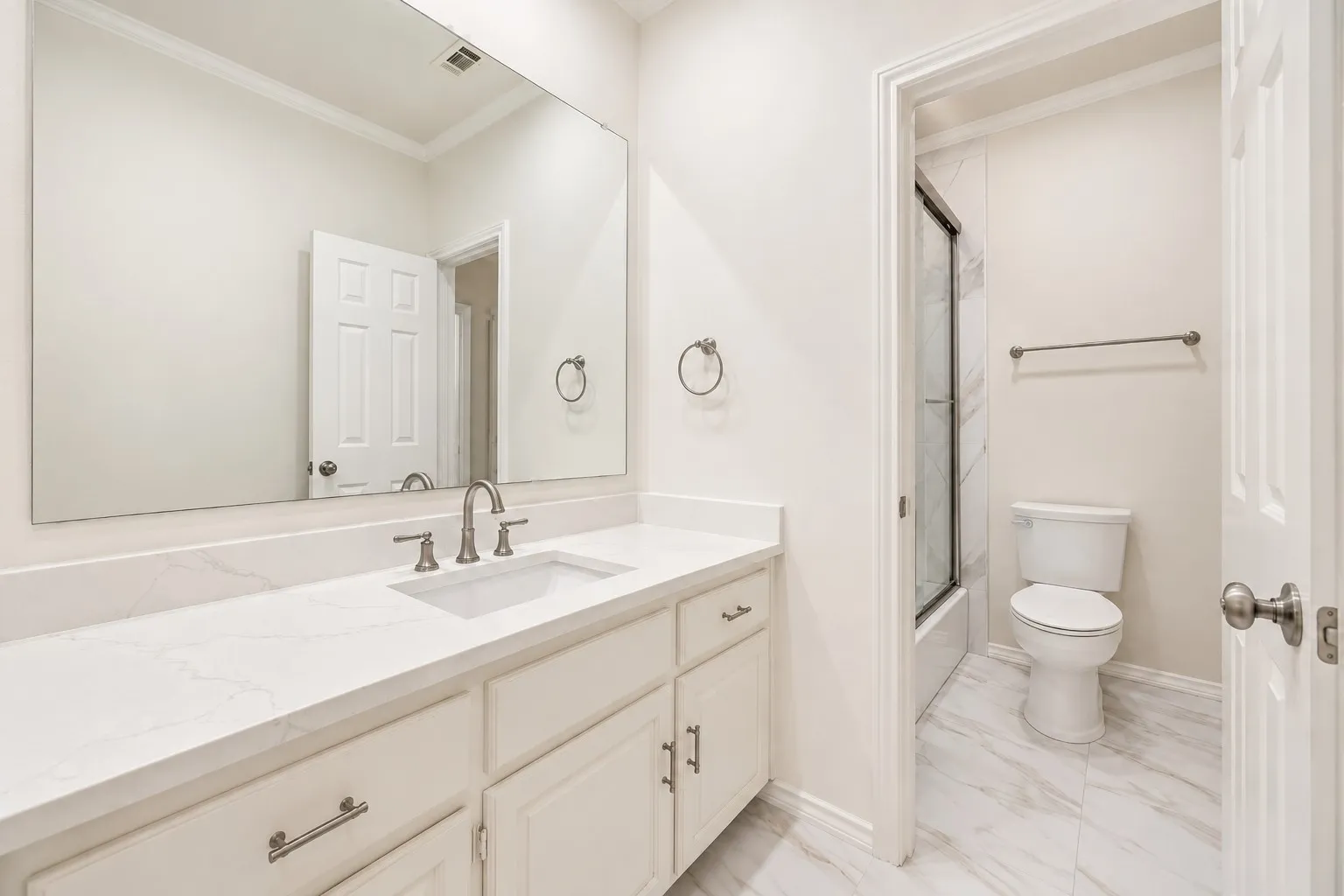 Vanity with a white countertop and undermount sink, brushed nickel faucet, large wall mirror, and white cabinetry