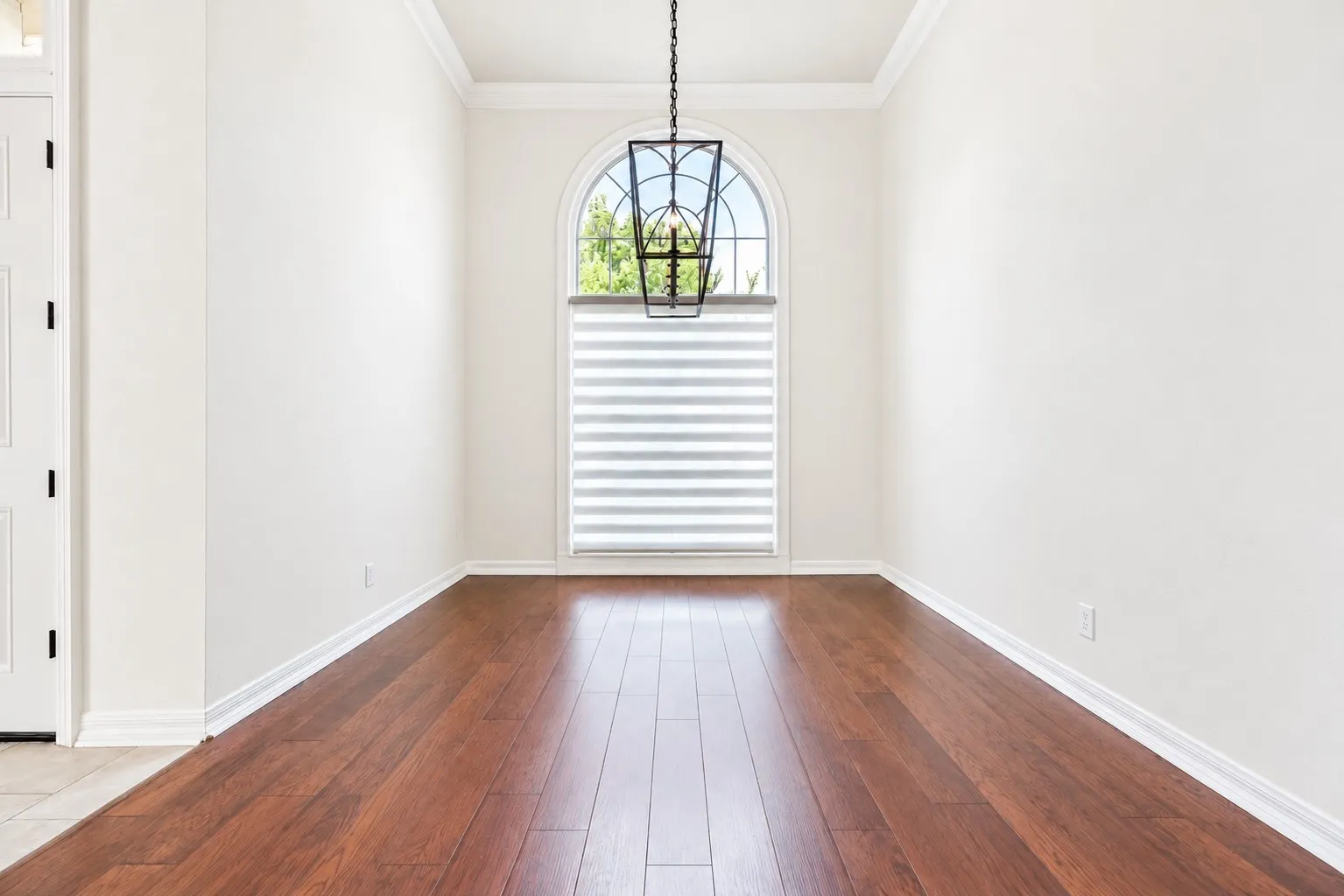 Arch-top window with layered shades, dark wood-finish flooring, and crown molding