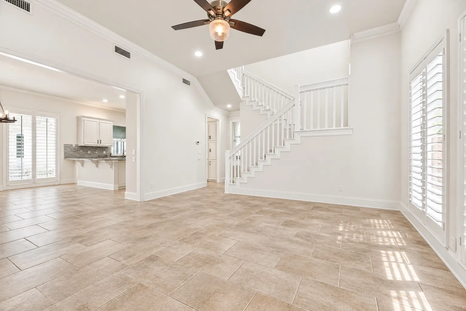 Open-concept living space featuring tiled flooring, a prominent staircase with white railings, and white plantation shutters on large windows