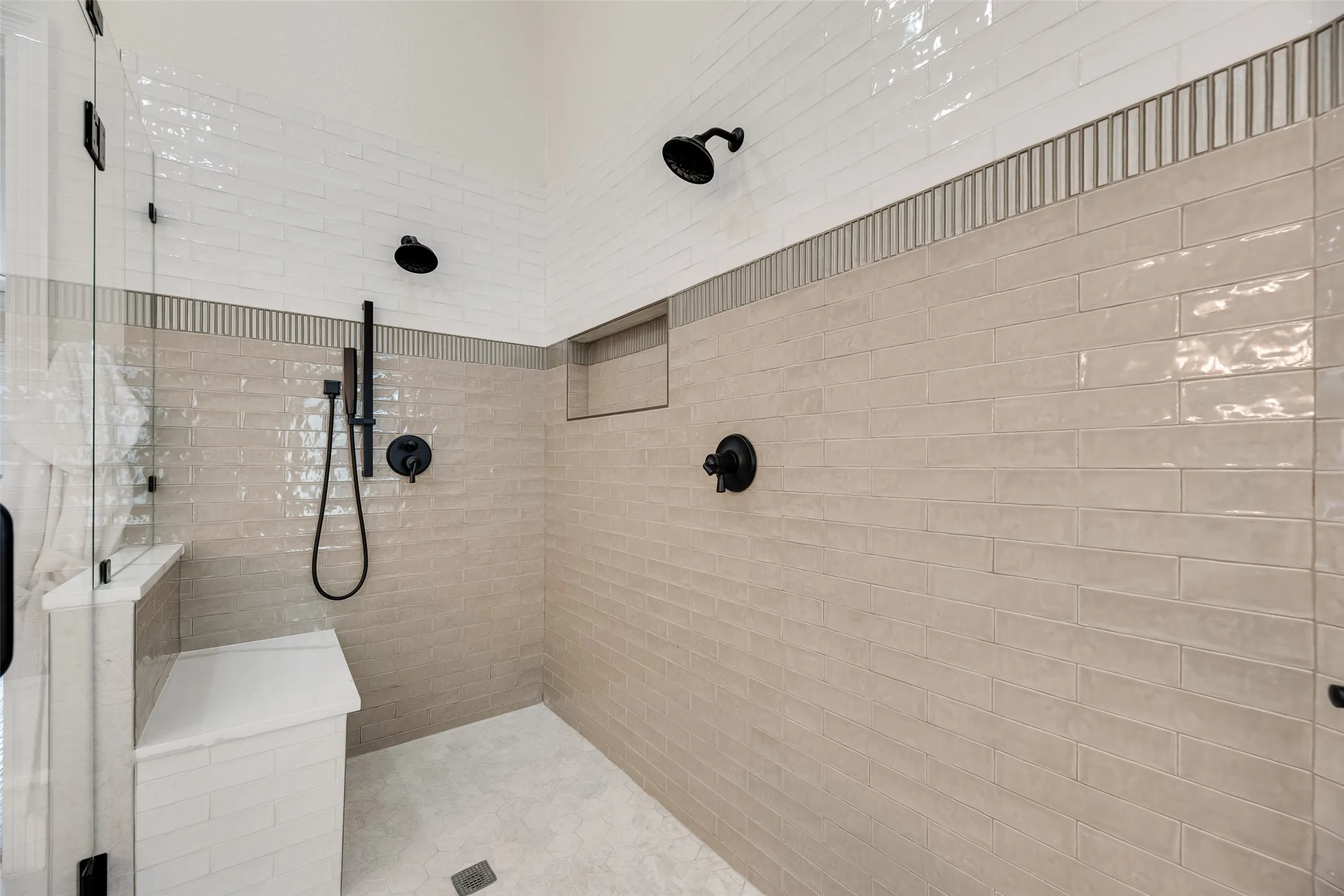 Walk-in shower with dual showerheads, matte black fixtures, built-in bench, and recessed shelf