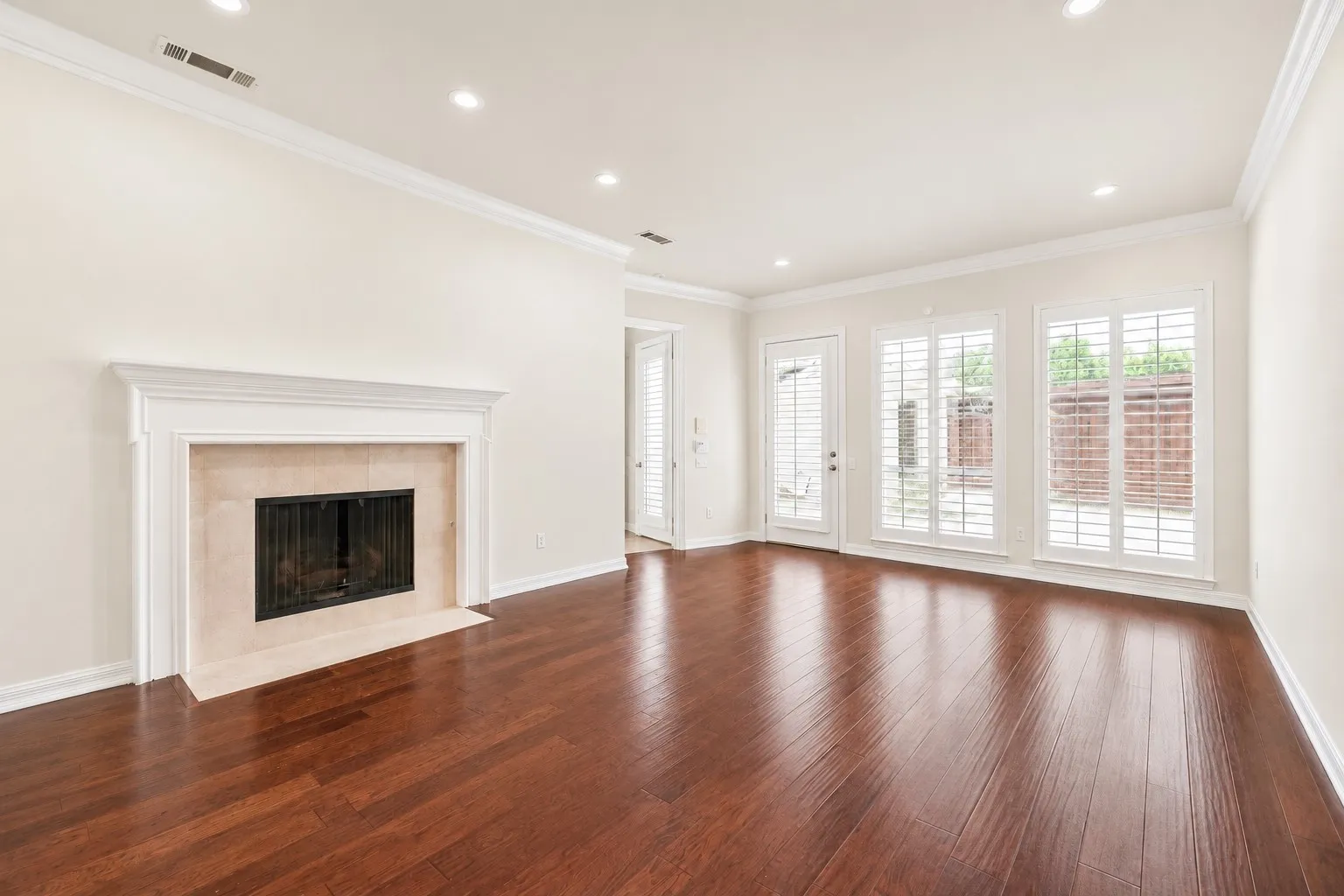 Hardwood flooring, recessed lighting, crown molding, fireplace with hearth, and multiple windows with plantation shutters