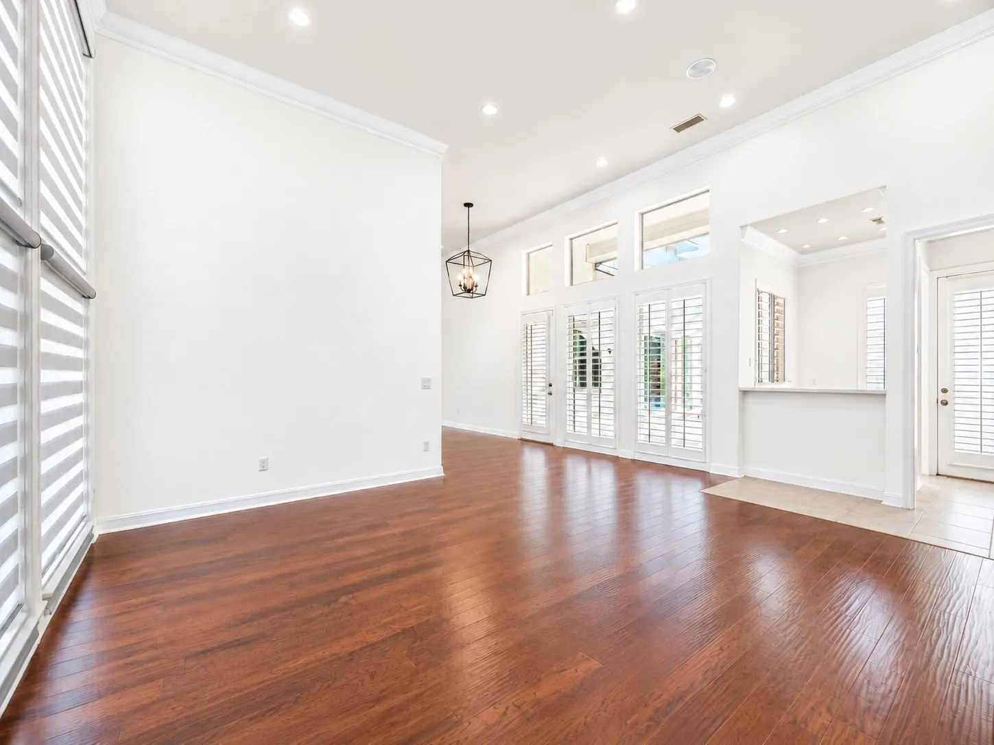 Wood-finish flooring, high ceilings with crown molding, recessed lighting, and a modern chandelier