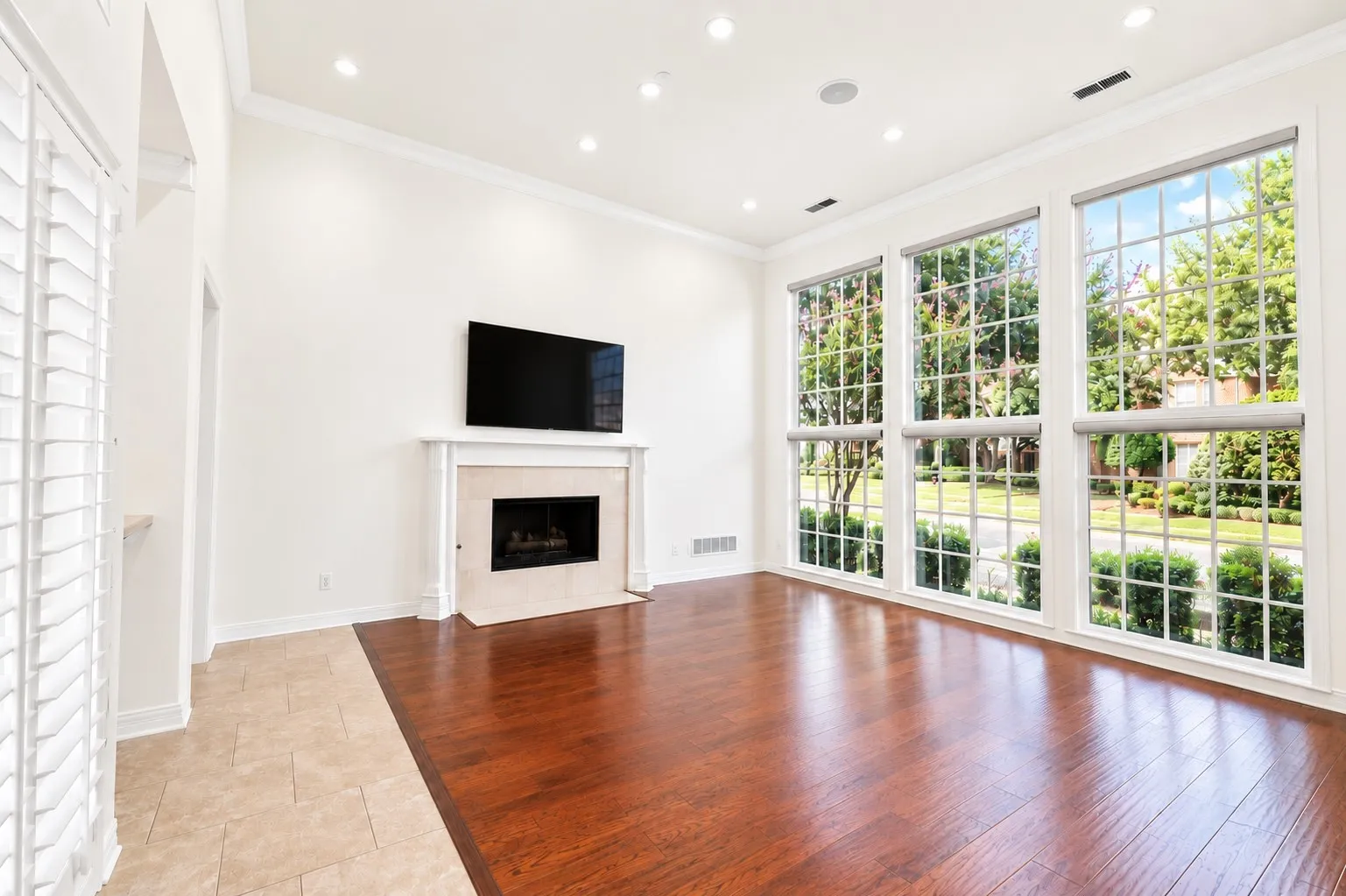 High ceilings with recessed lighting, a built-in fireplace with a stone surround, rich wood-finish flooring, and large picture windows with grids