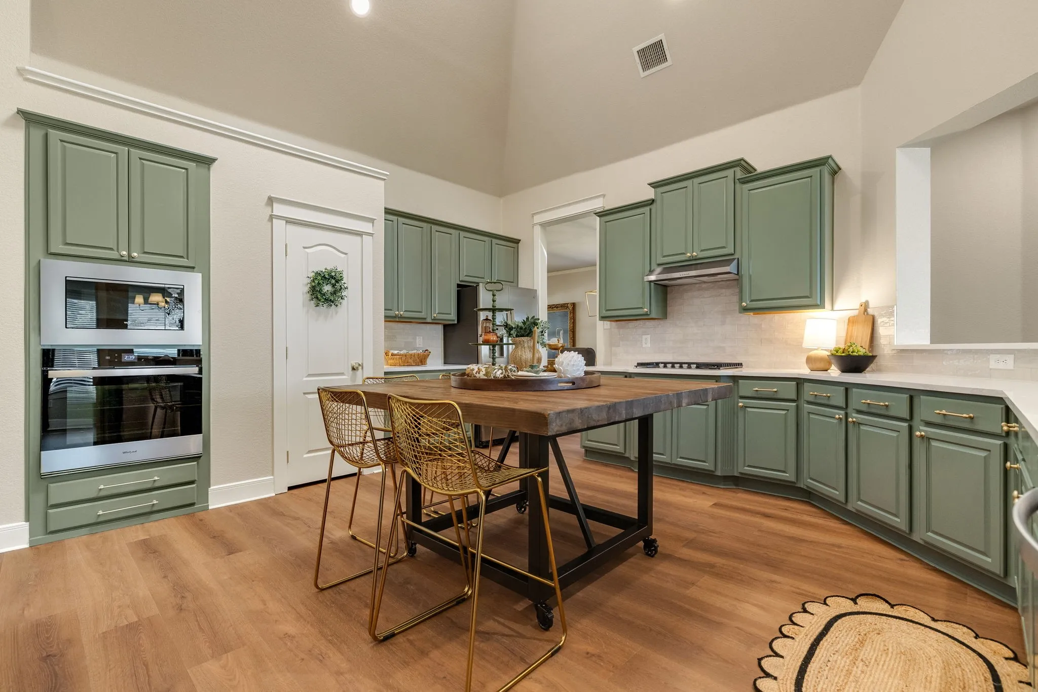 Vaulted ceiling kitchen featuring green cabinetry, stainless steel built-in appliances, light-toned countertops, tile backsplash, and wood-finish flooring