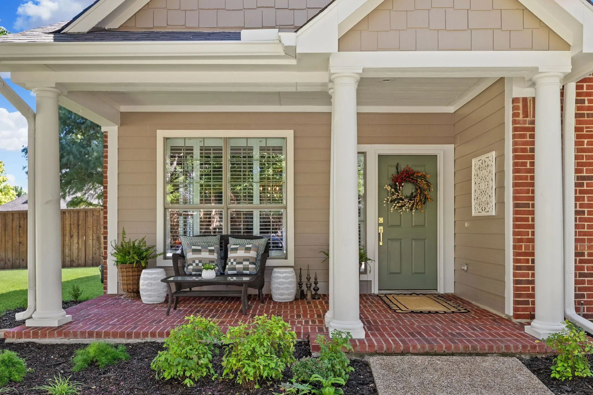 Covered front porch with brick flooring, decorative columns, and a paneled entry door