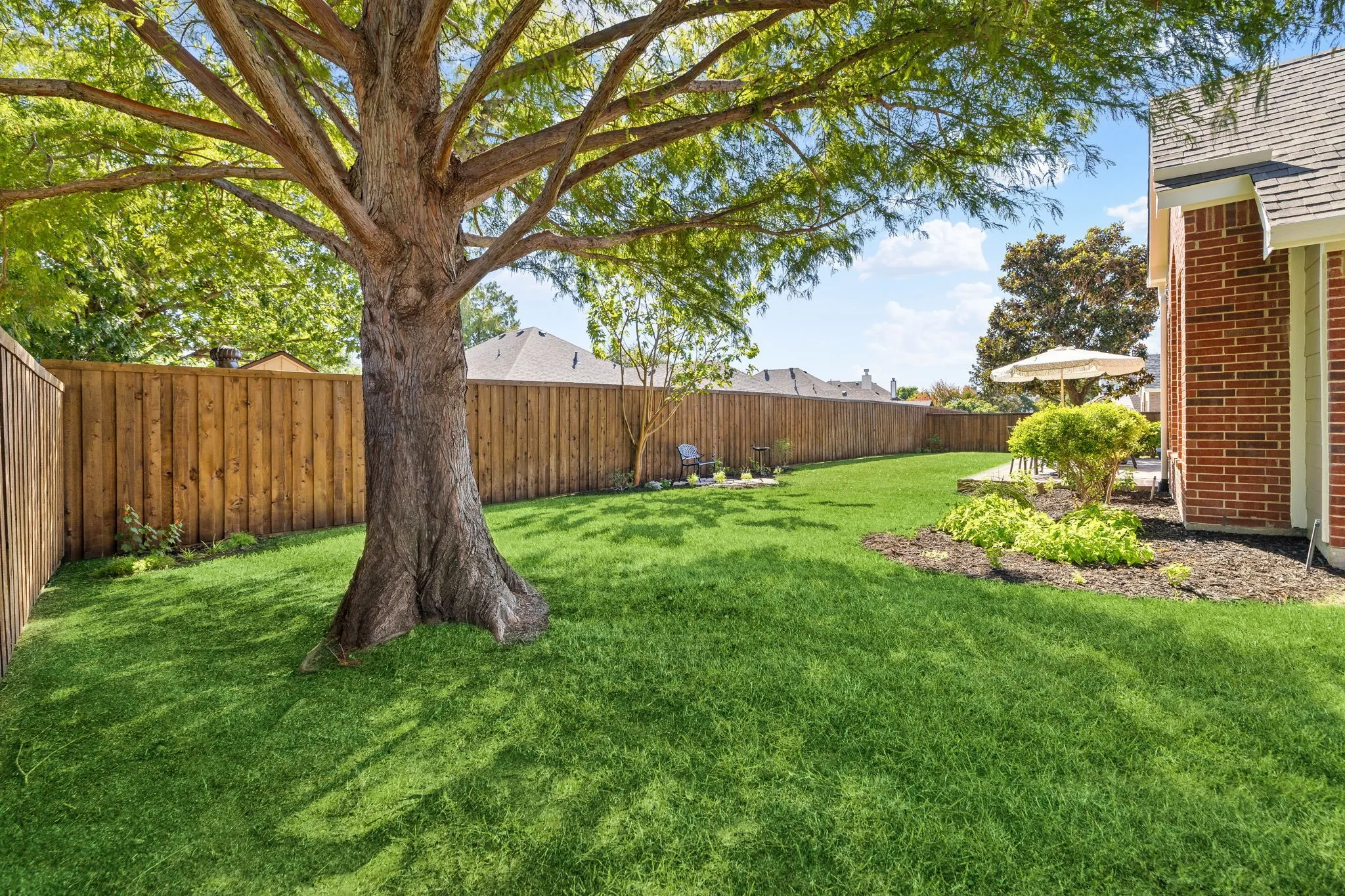 Expansive green lawn with a mature tree, solid wood fencing, and a brick exterior