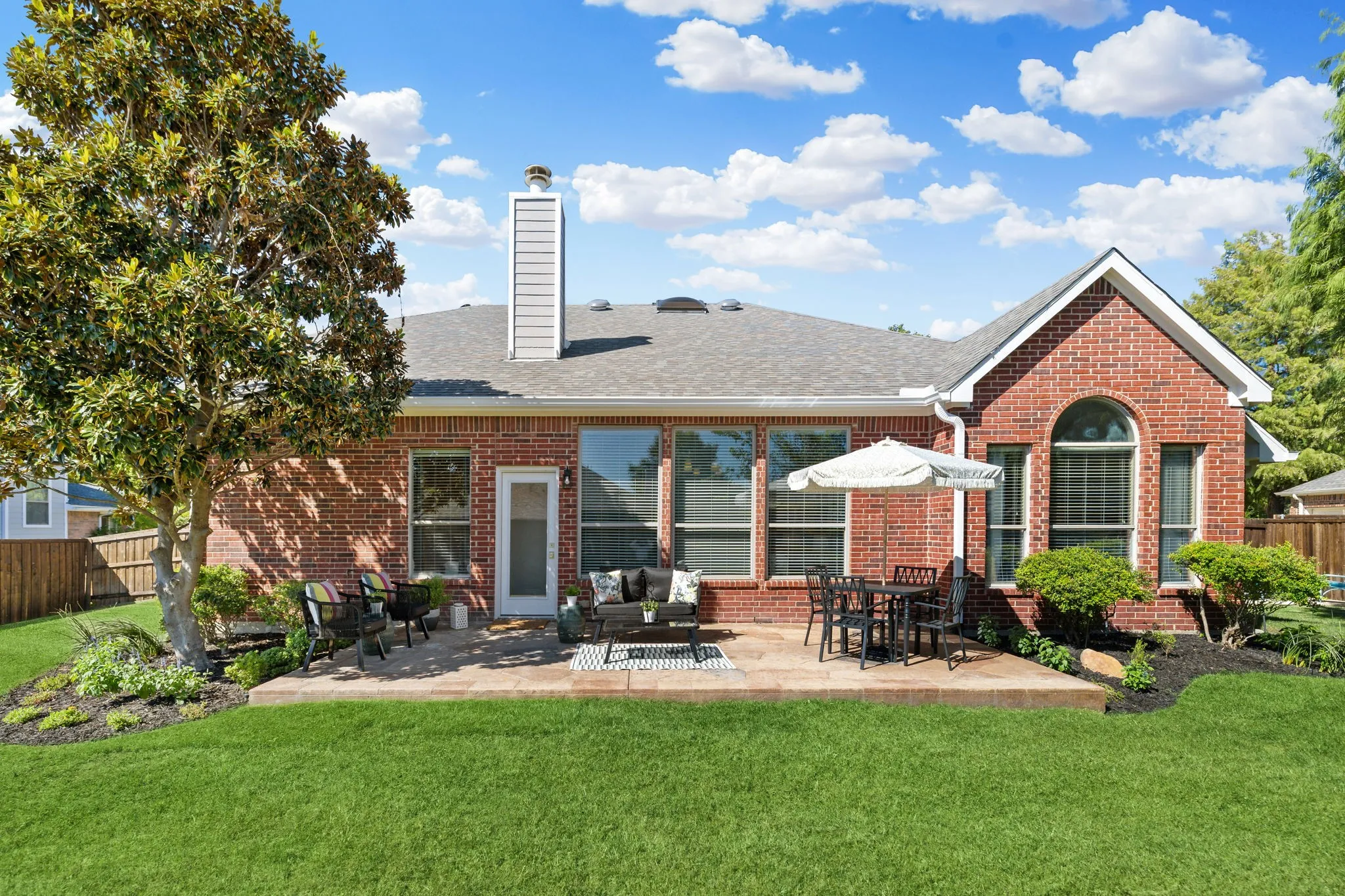 Brick exterior, expansive lawn, paved patio, mature landscaping, and multiple large windows