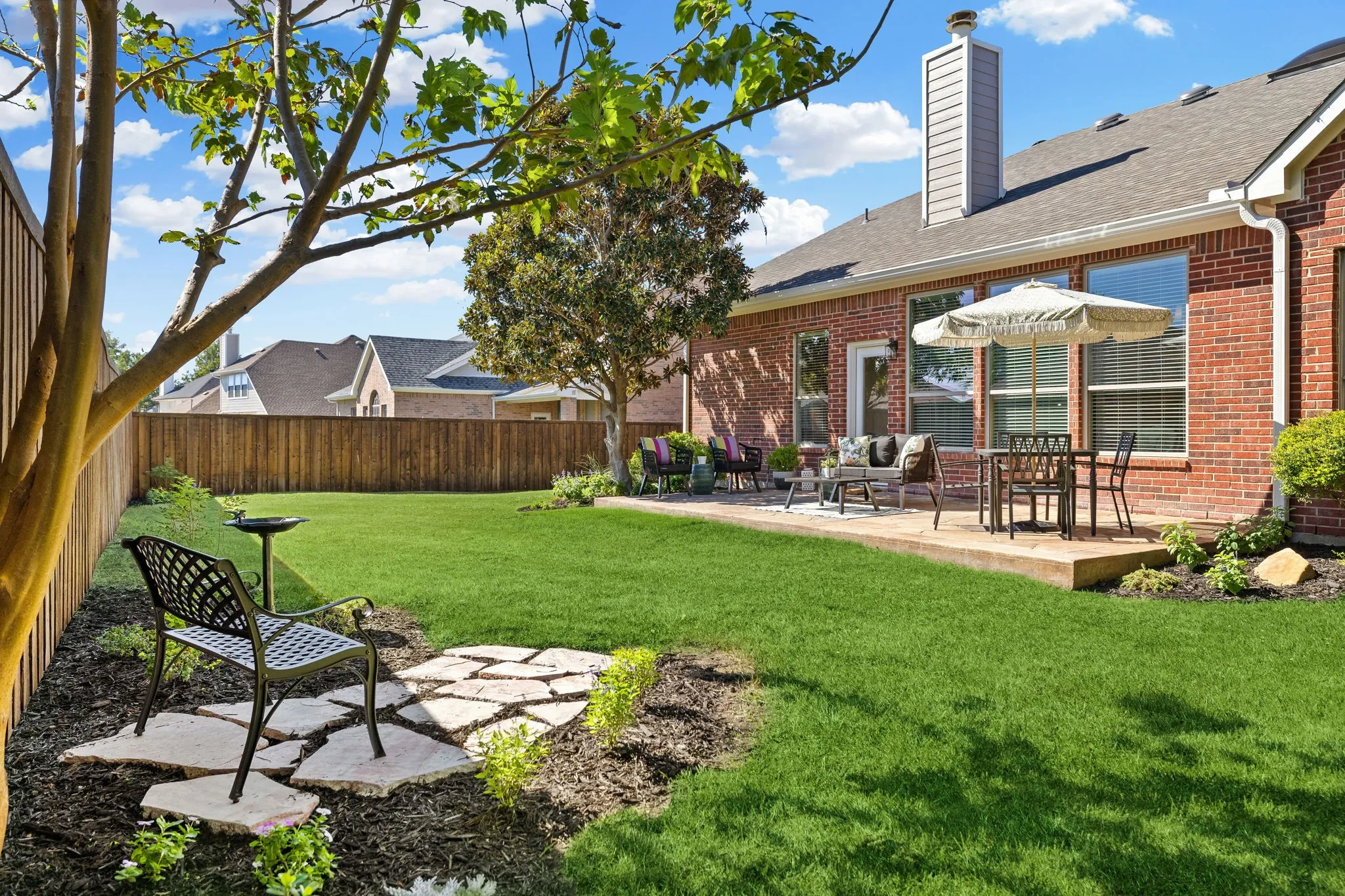 Expansive green lawn with a wood fence, concrete patio, and mature trees