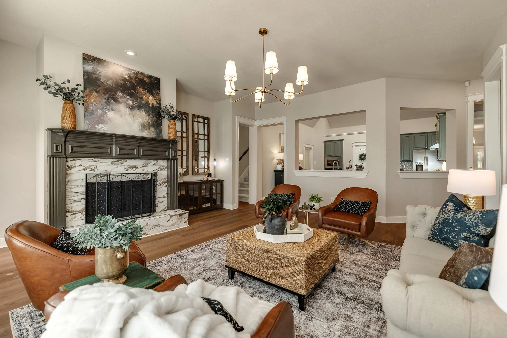 Wood-finish flooring, a fireplace with a decorative mantel and stone surround, and an overhead multi-arm chandelier