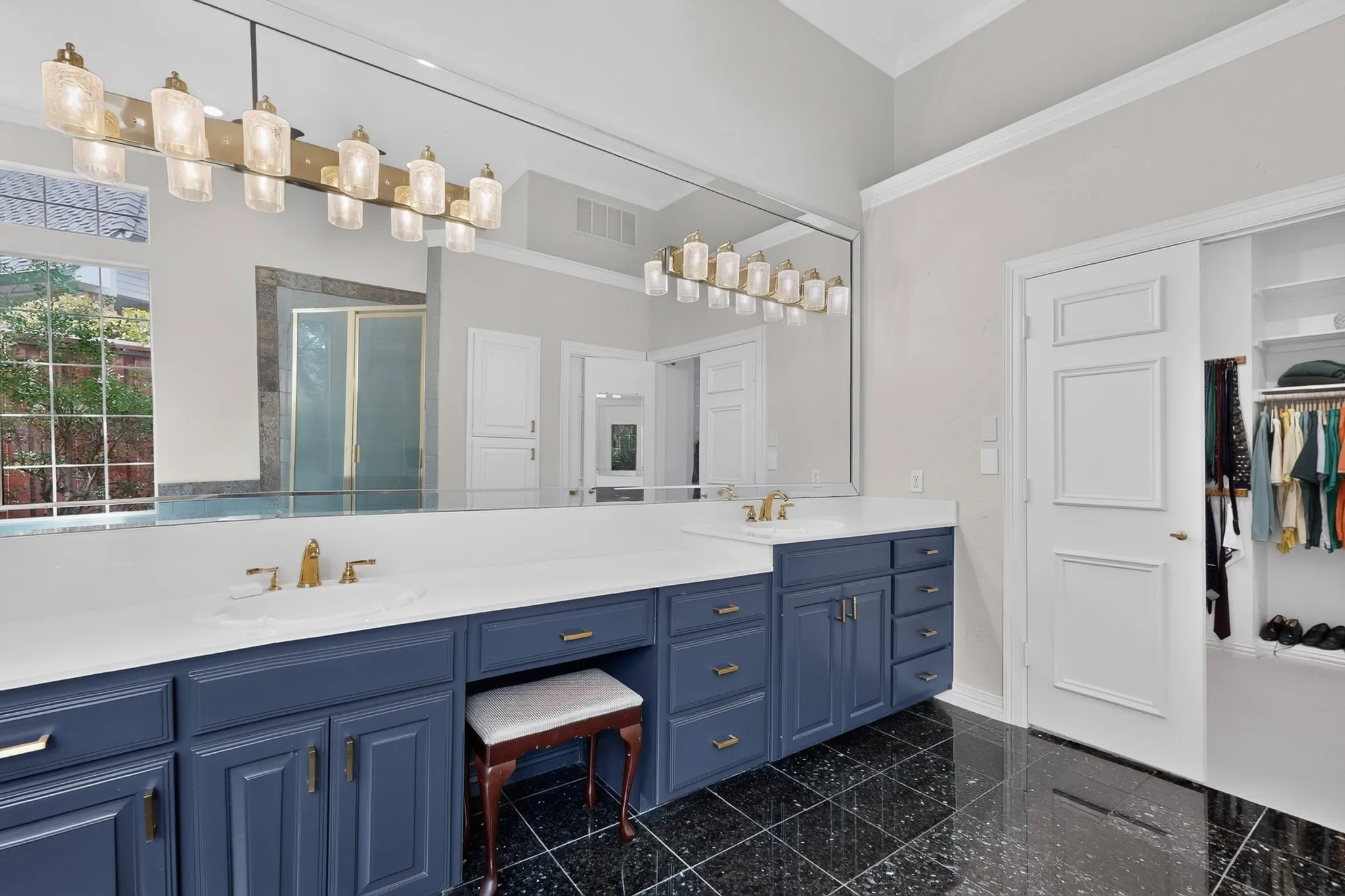 Bathroom featuring a large vanity with dual sinks, blue cabinetry, white countertops, a full-width mirror, and black tile flooring