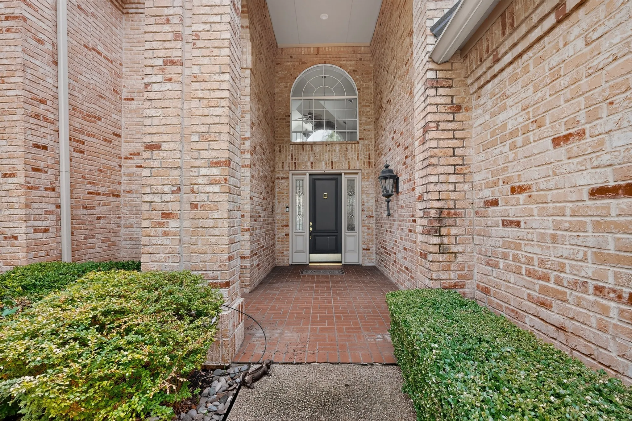 Brick exterior with a covered entry, arched transom window, black paneled front door with sidelights, and a brick paver porch