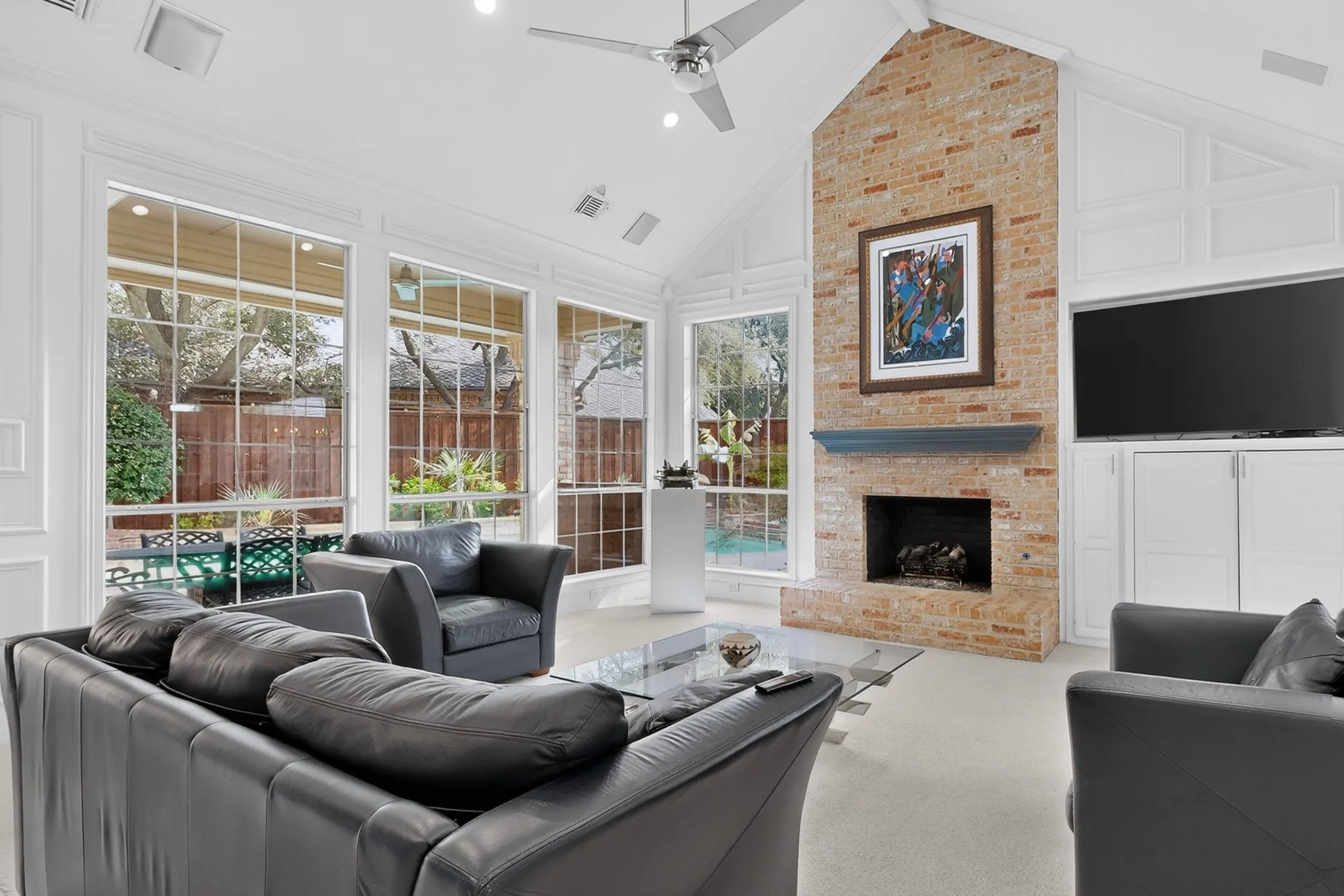 Vaulted ceiling with exposed beam, full-height brick fireplace, built-in cabinetry, and expansive windows