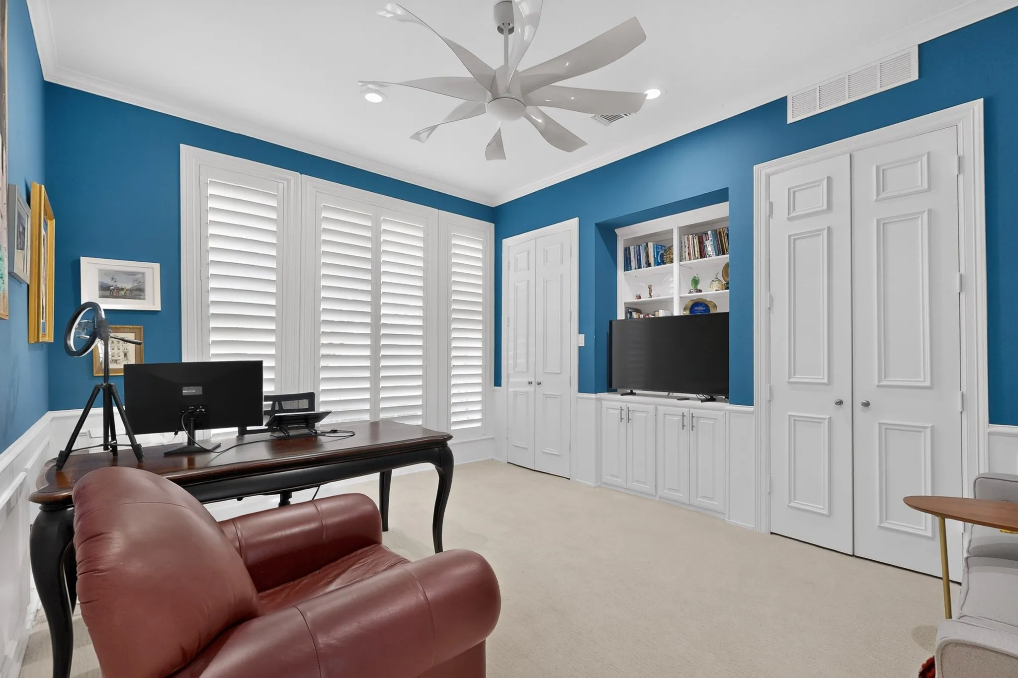 Custom built-in shelving, white plantation shutters, decorative panel doors, crown molding, and a modern ceiling fan with integrated lighting