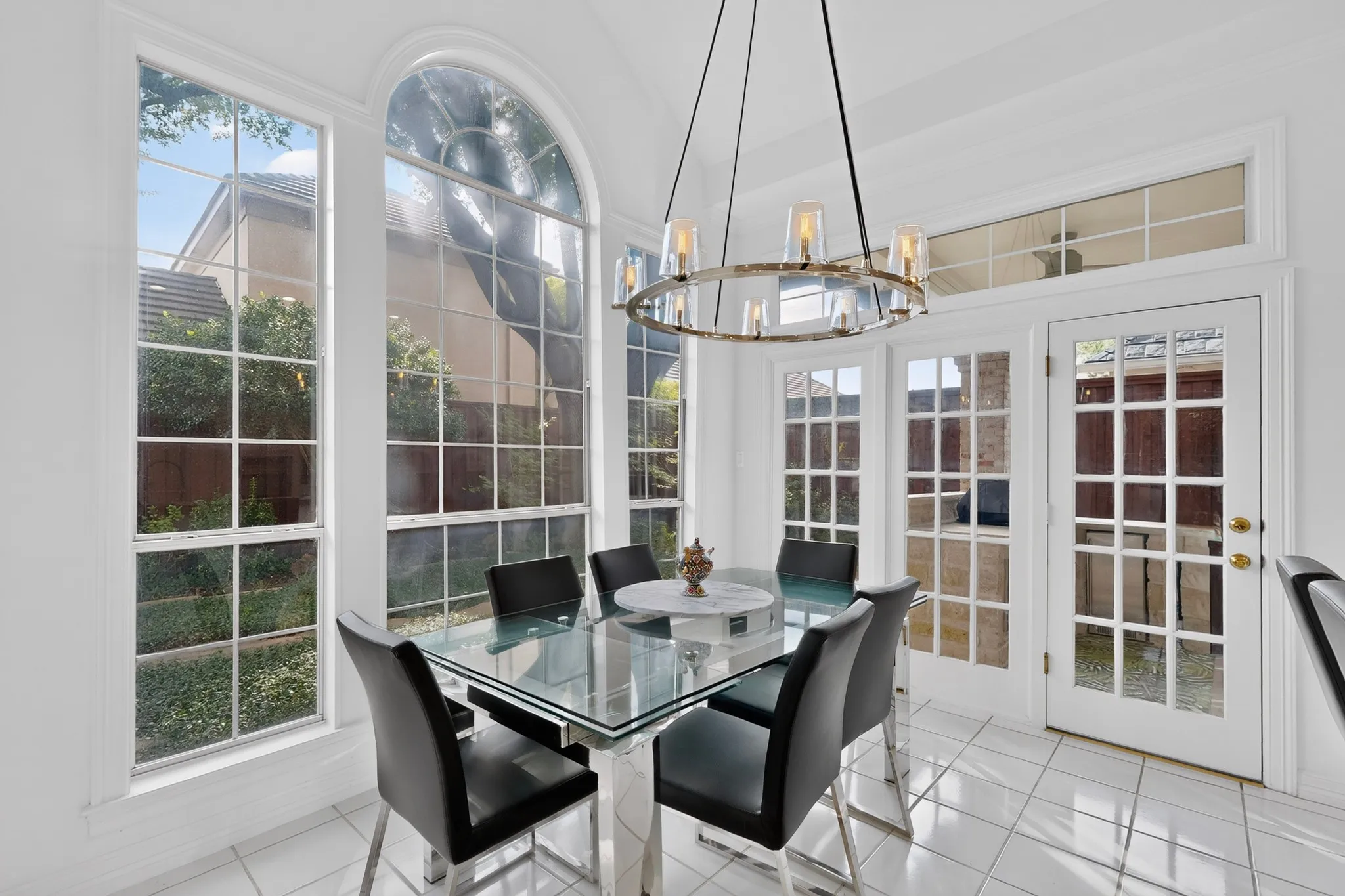 Vaulted ceiling with an ornate chandelier, arched window, French doors, and tile flooring