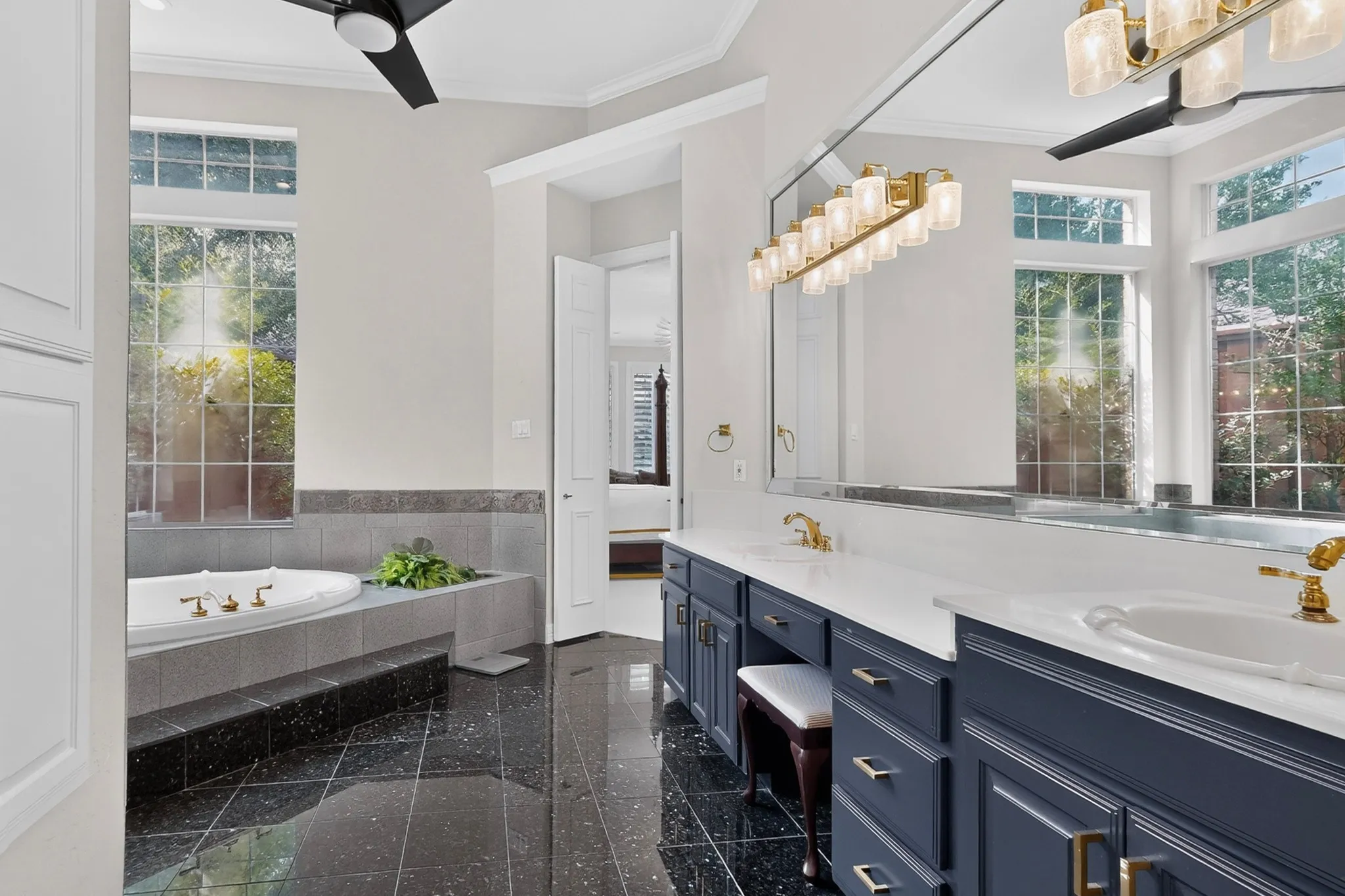 Soaking tub with surrounding tile, dual vanity with white countertops, black tile flooring, and two ceiling fans
