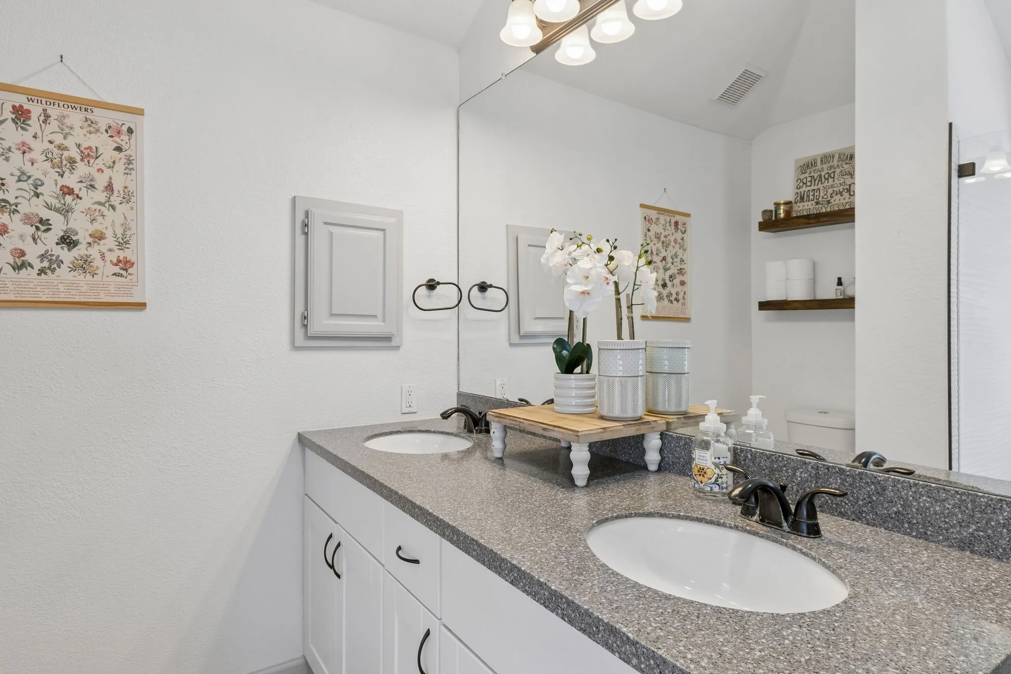 Another view of the primary showing the vanity with dual sinks, a smooth stone countertop and a large mirror.