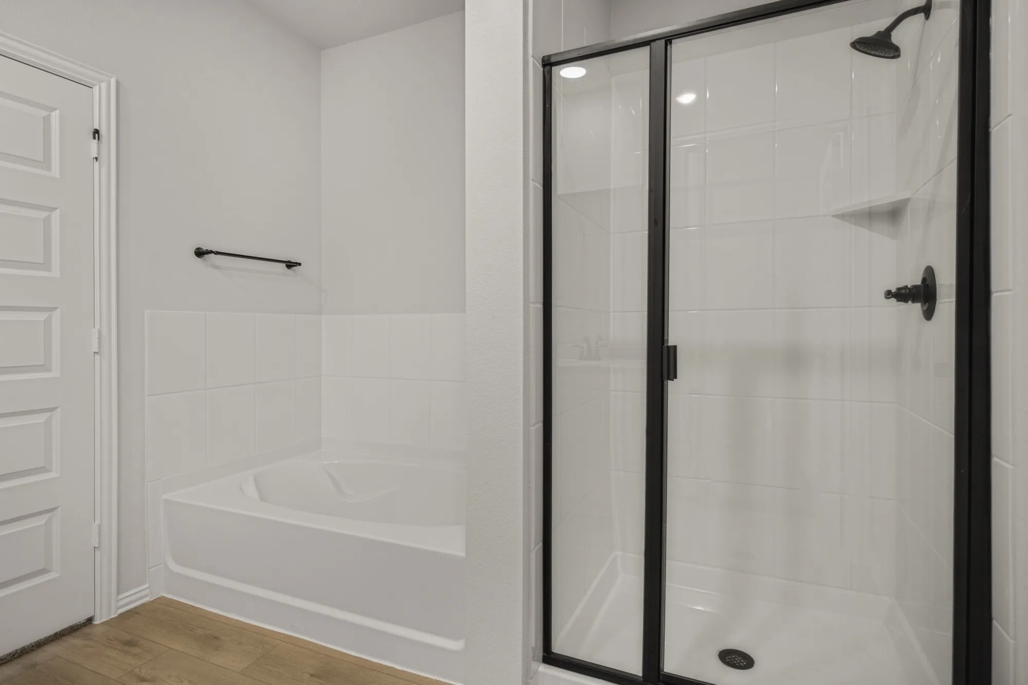 Walk-in shower with clear glass enclosure and matte black fixtures, white tiled walls, and a corner bathtub