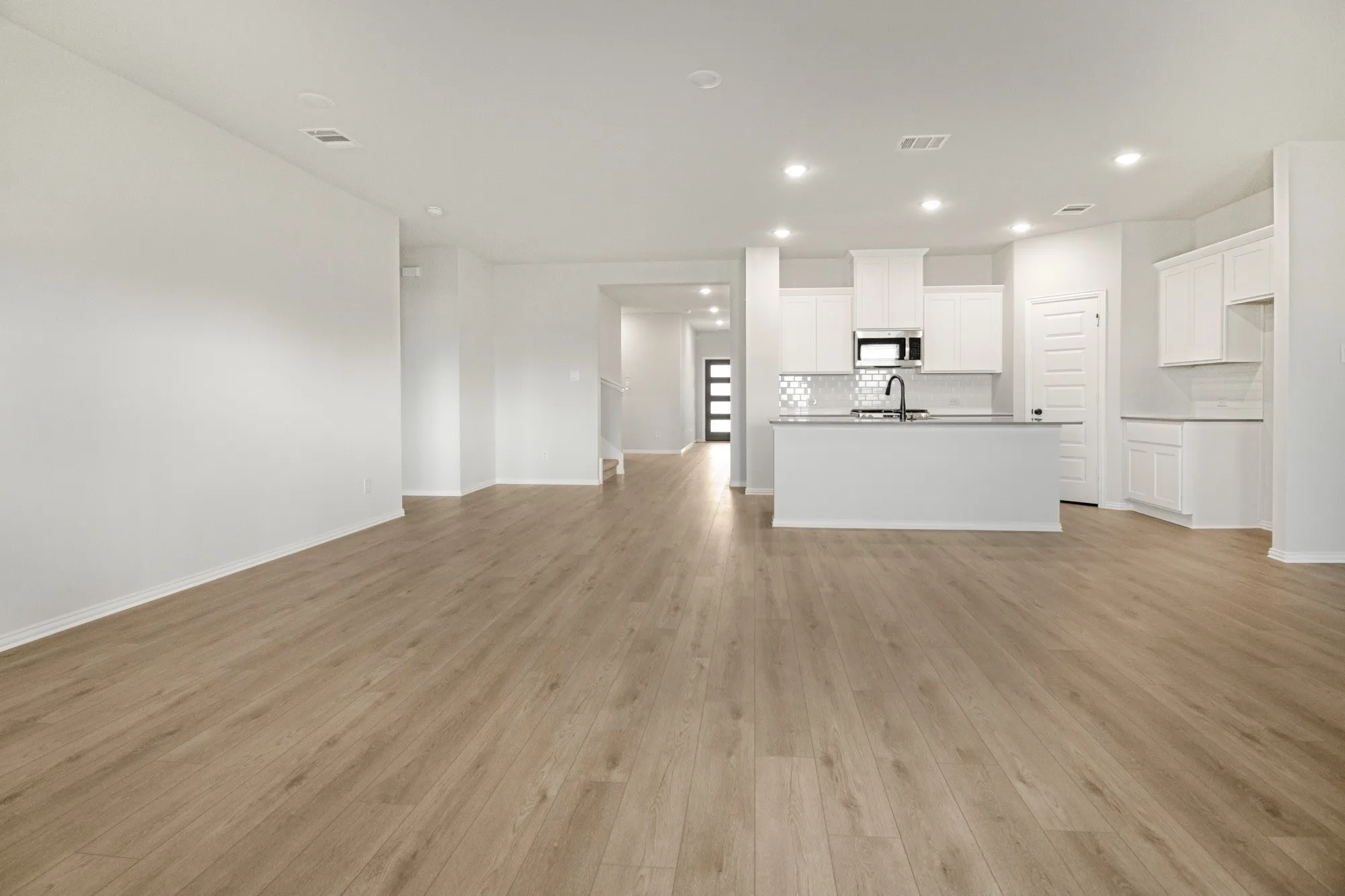 Wood-finish flooring throughout, white cabinetry, island with integrated sink, white subway tile backsplash, and recessed lighting