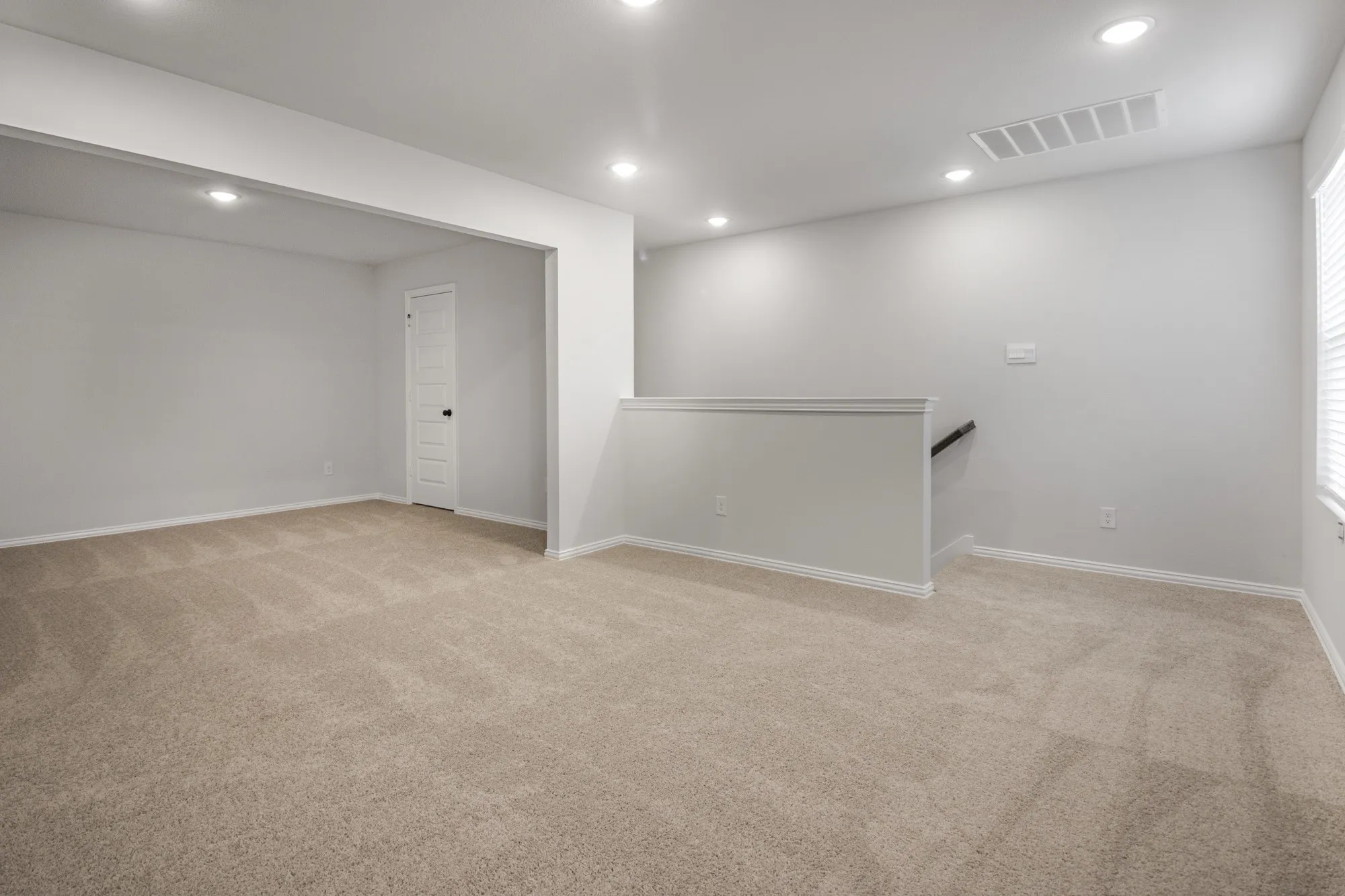 Recessed lighting illuminates the neutral-toned carpeted flooring and light gray walls