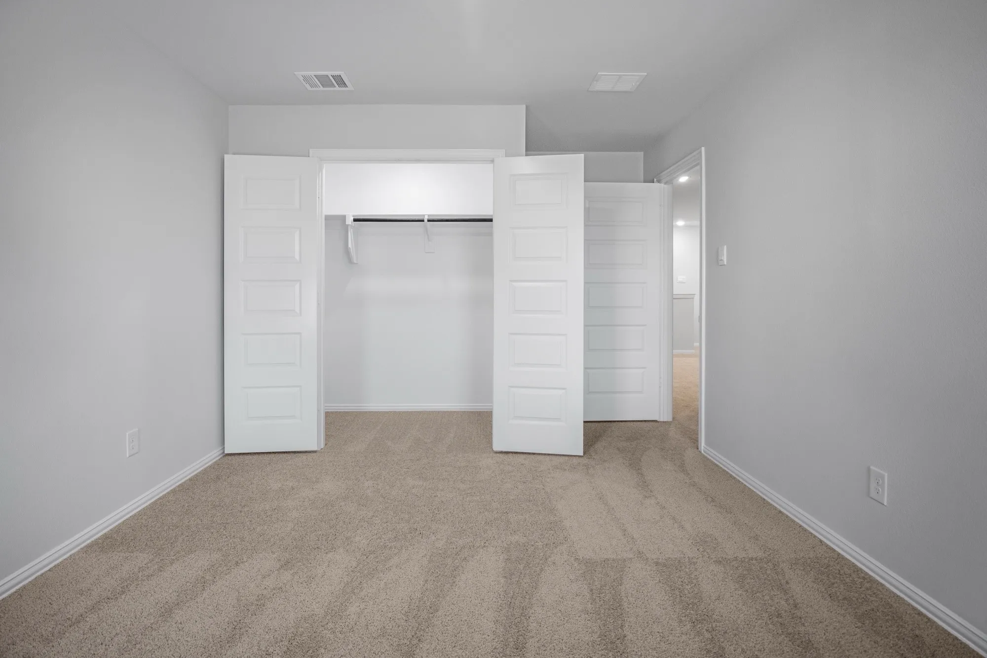 Carpeted flooring with light gray walls, featuring a closet with bi-fold doors and a hanging rod