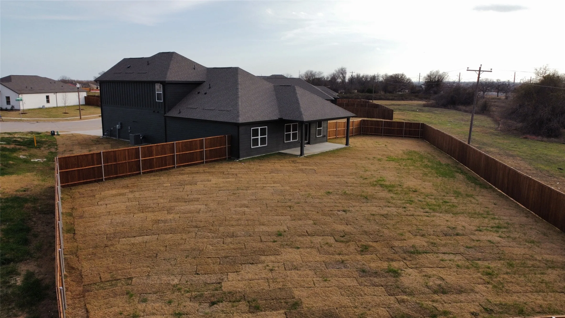 Expansive lot featuring a newly installed wooden privacy fence, a concrete patio, and a shingle roof