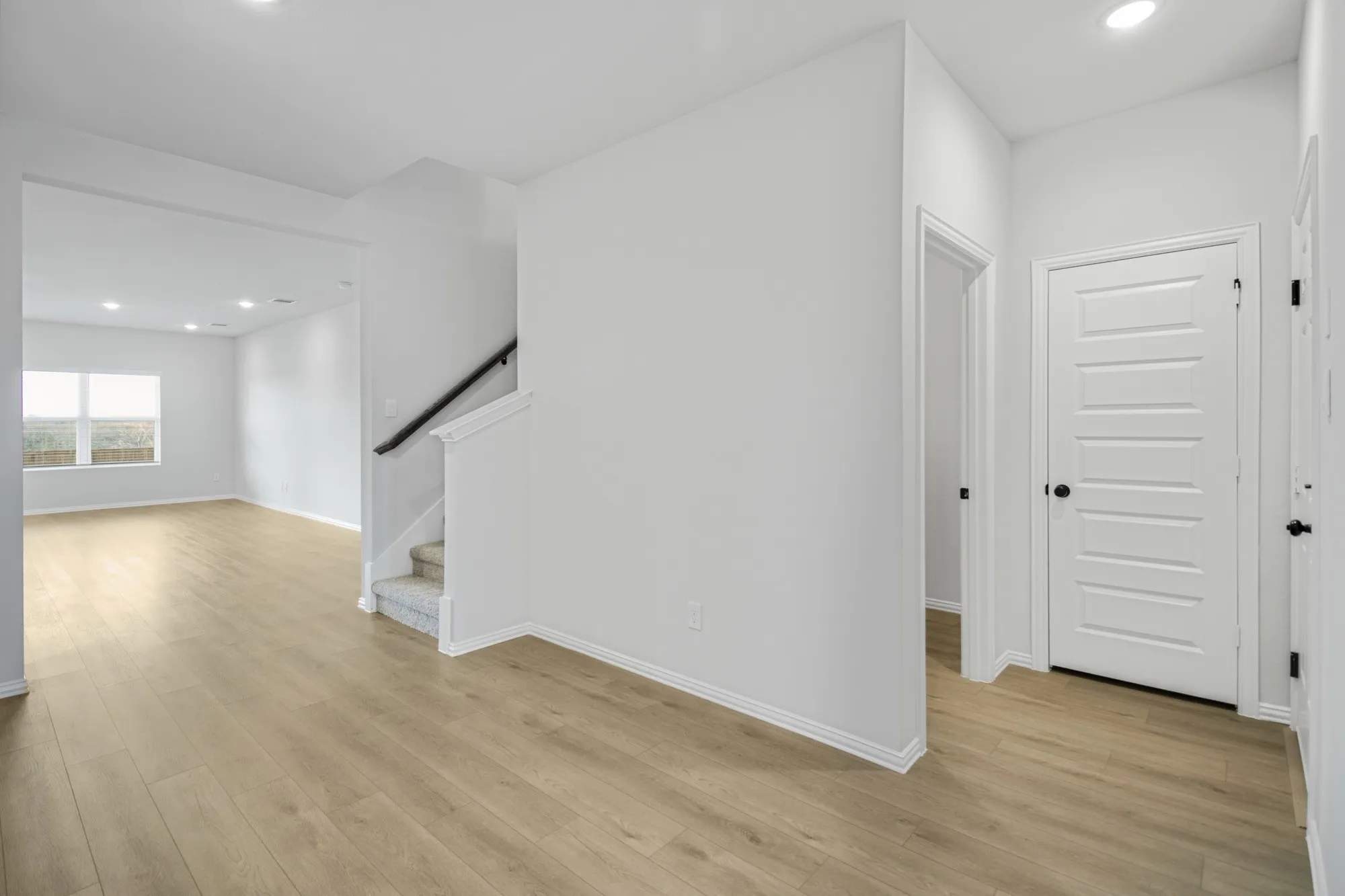 Open-concept living area with light wood-finish flooring, recessed lighting, and a neutral color palette