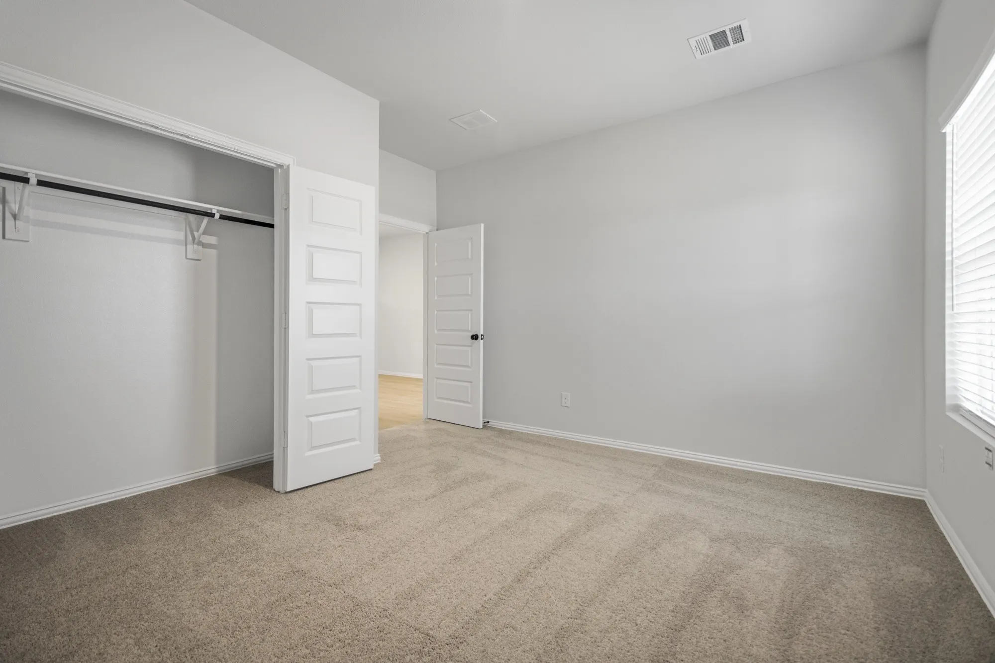 Neutral wall color, wall-to-wall carpeting, window with blinds, and a built-in closet with hanging rod