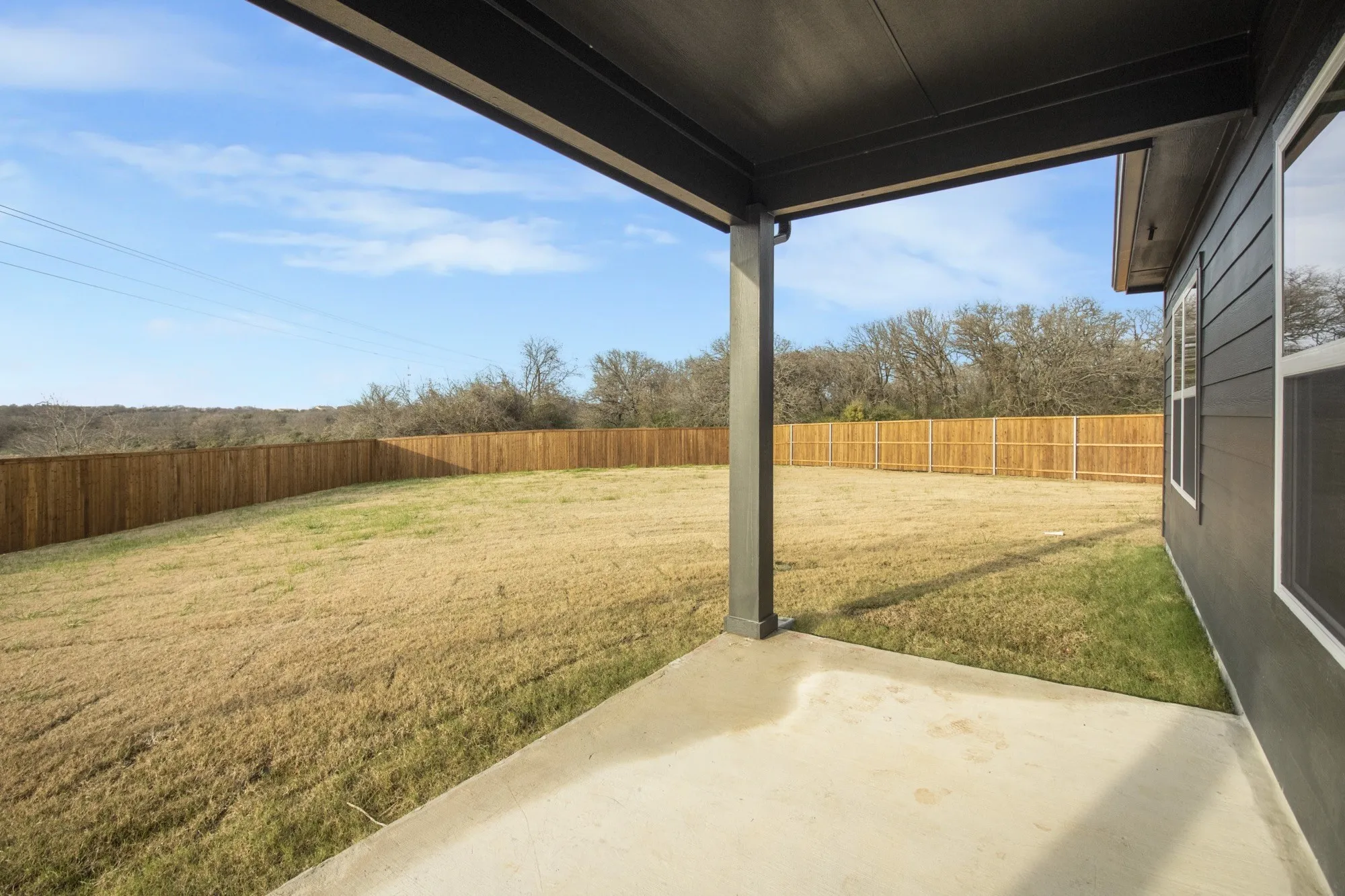 Expansive backyard featuring a wood fence, concrete patio, and covered patio area