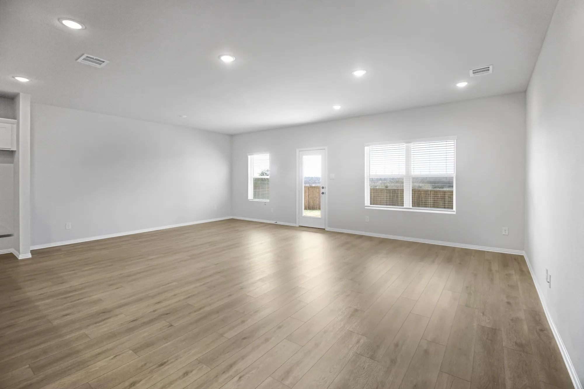 Recessed lighting, wood-finish flooring, white walls, multiple windows with blinds, and an exterior door