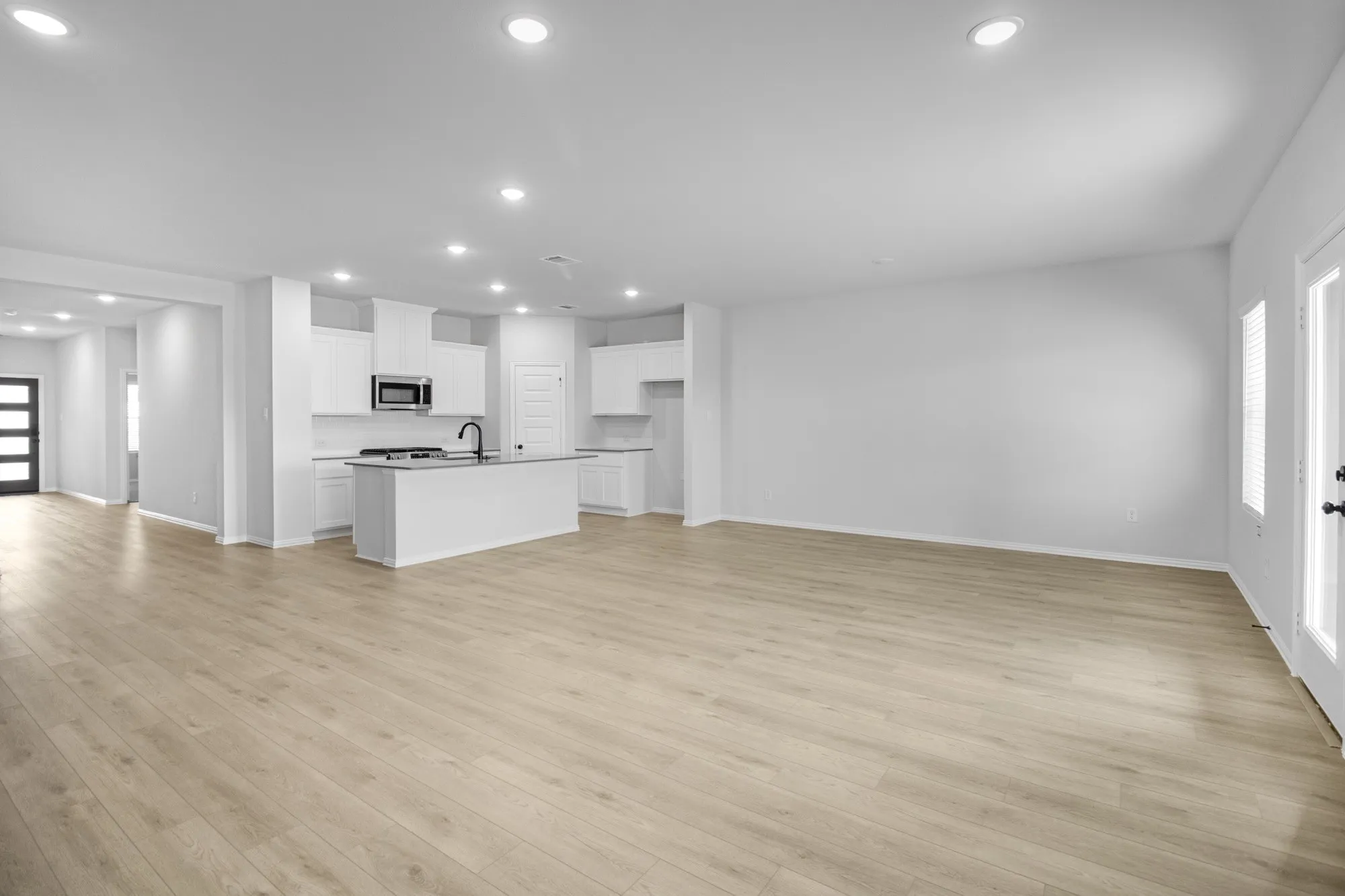 Open-concept living area featuring wood-finish flooring, recessed lighting, and a kitchen with white cabinetry, stainless steel appliances, and a central island with a sink