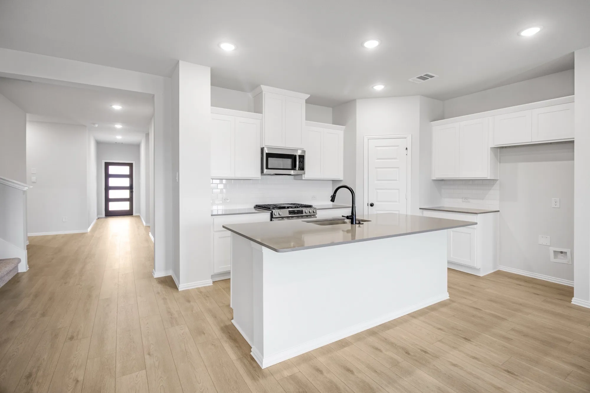 Kitchen featuring white cabinetry, a central island with a sink, stainless steel appliances, and wood-finish flooring