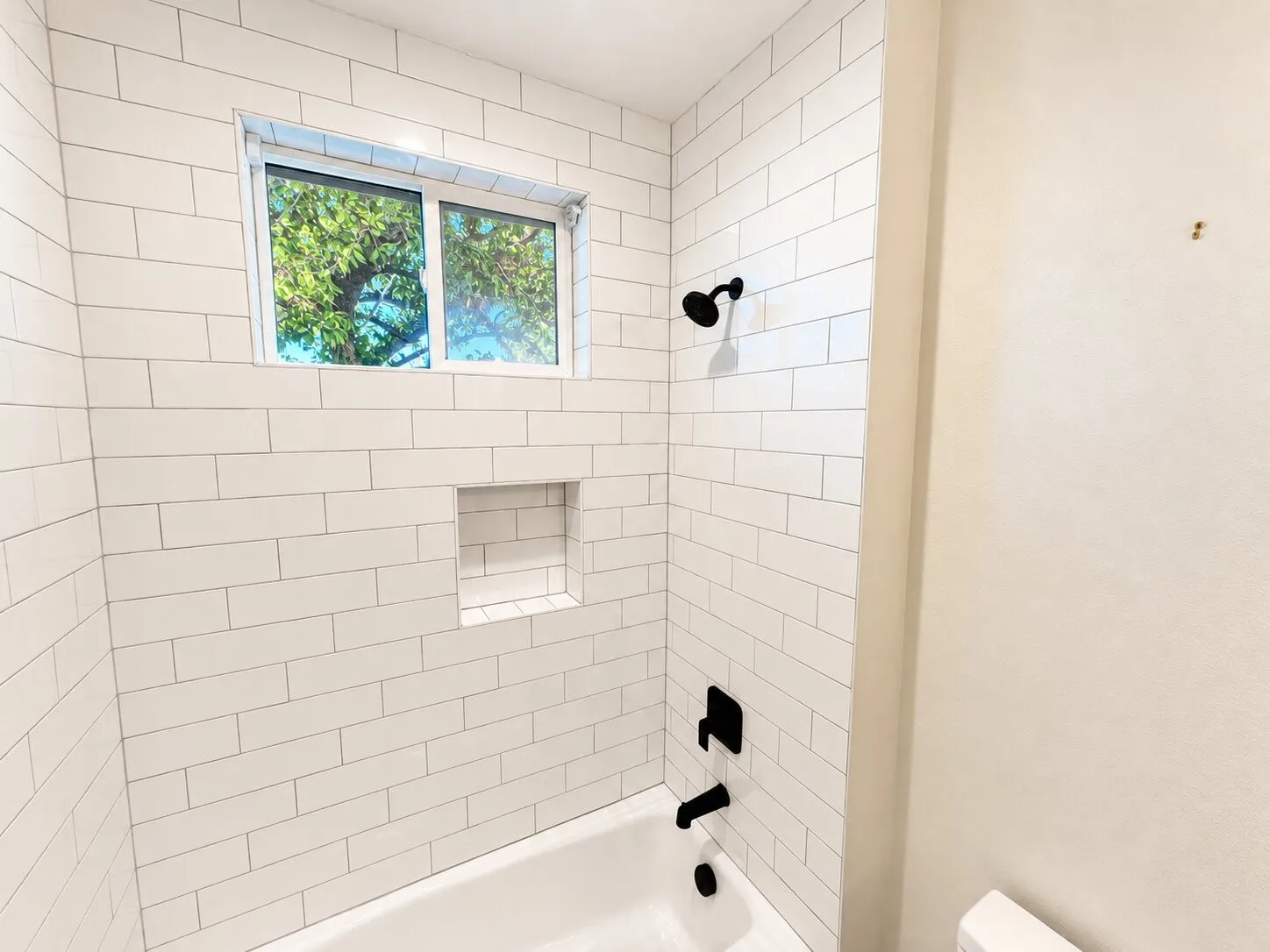 White subway tile shower surround featuring a built-in niche, black fixtures, and a white bathtub