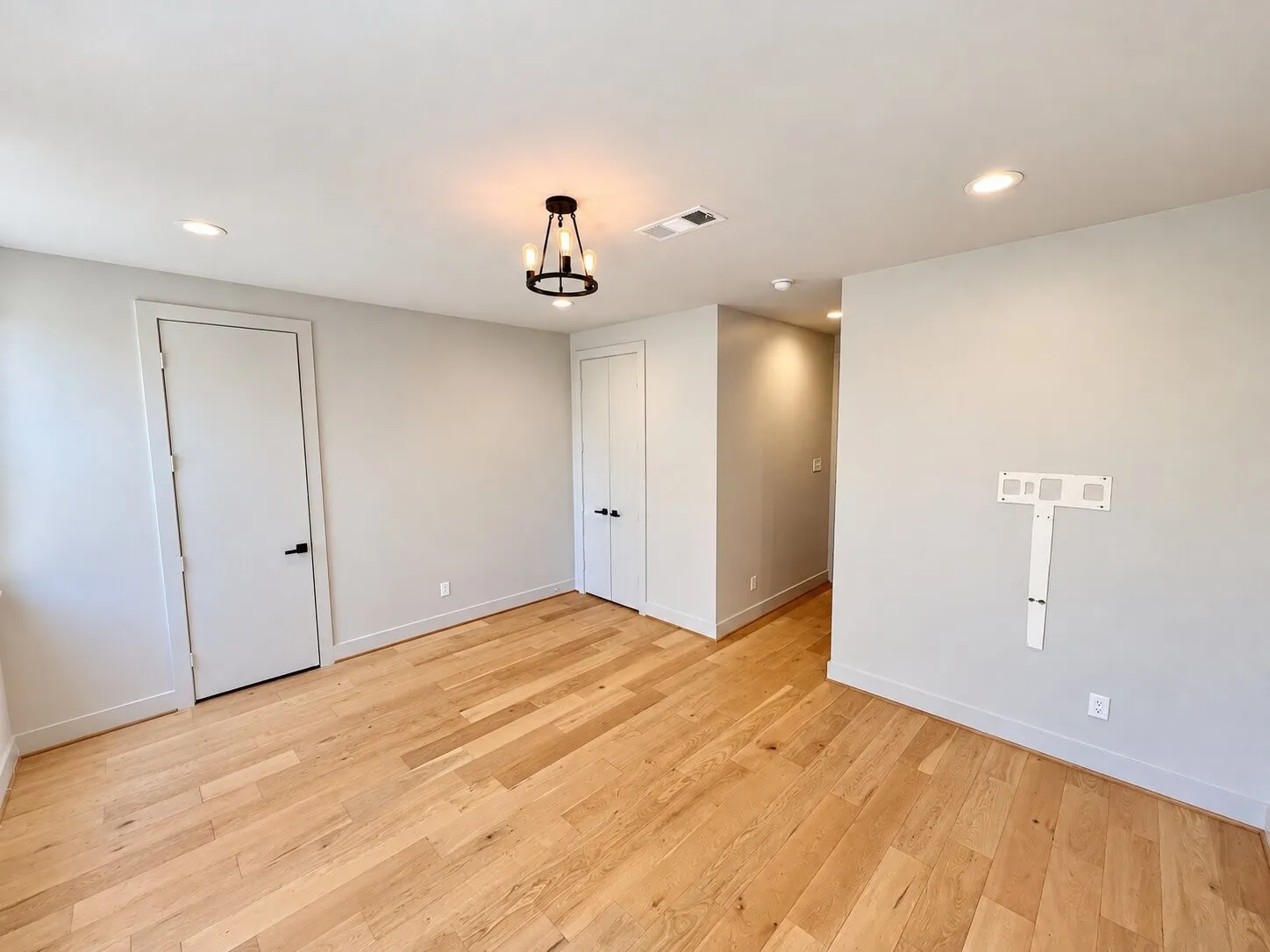 Light wood-finish flooring, recessed ceiling lighting, a modern chandelier, and two panel doors with matte black hardware