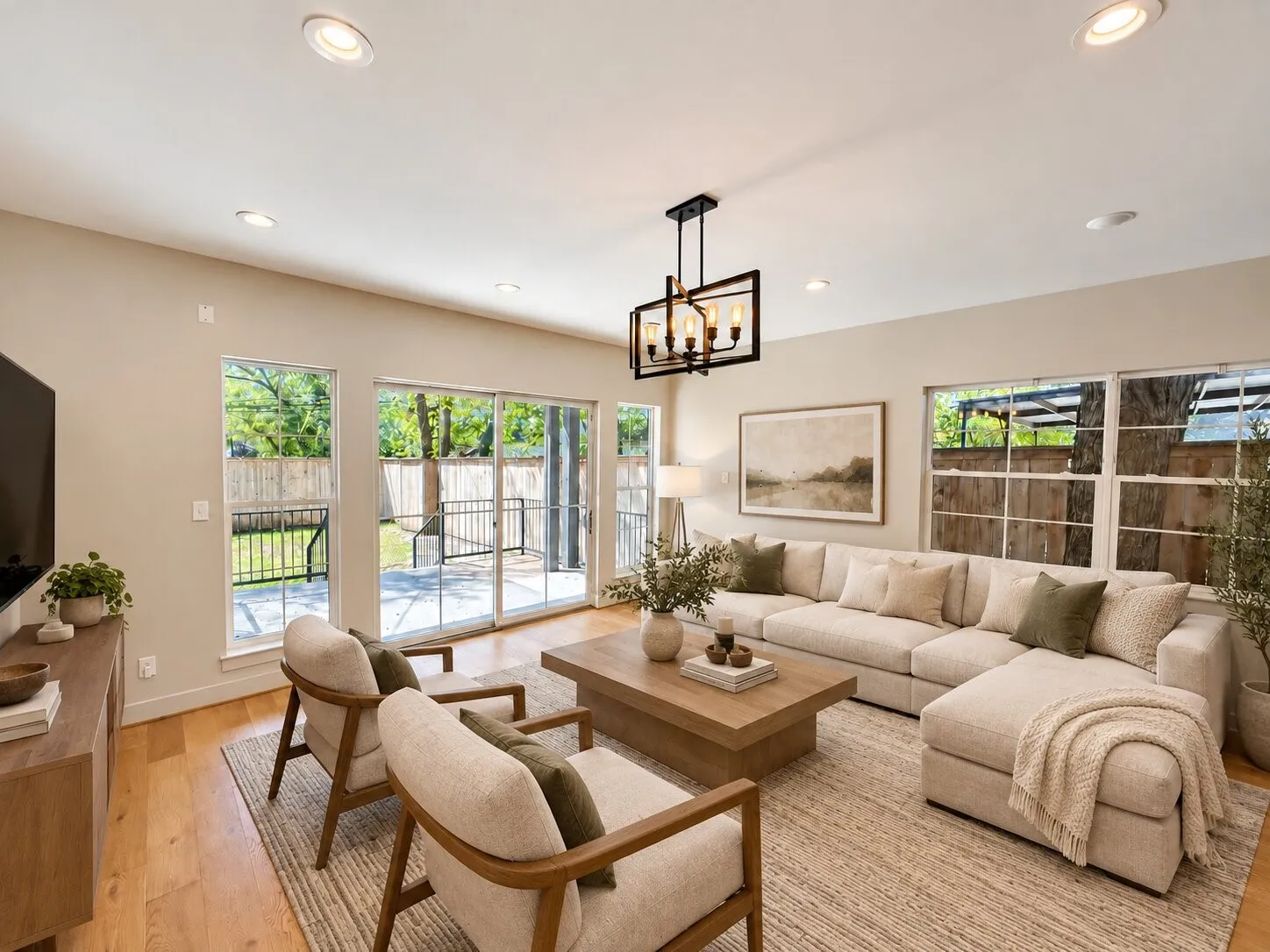 Virtually staged -
Bright, light-filled living room featuring multiple glass doors and windows with wood-finish flooring, recessed ceiling lighting, and a pendant fixture