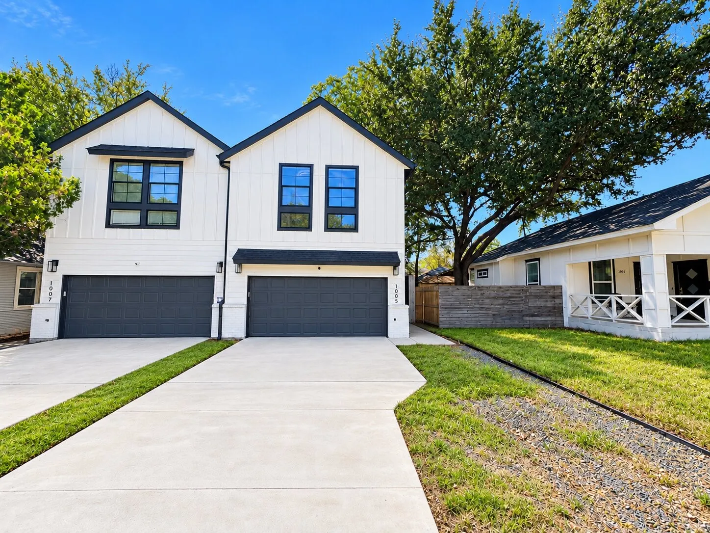 Contemporary duplex exterior with white siding, black-framed windows, and dark gray garage doors